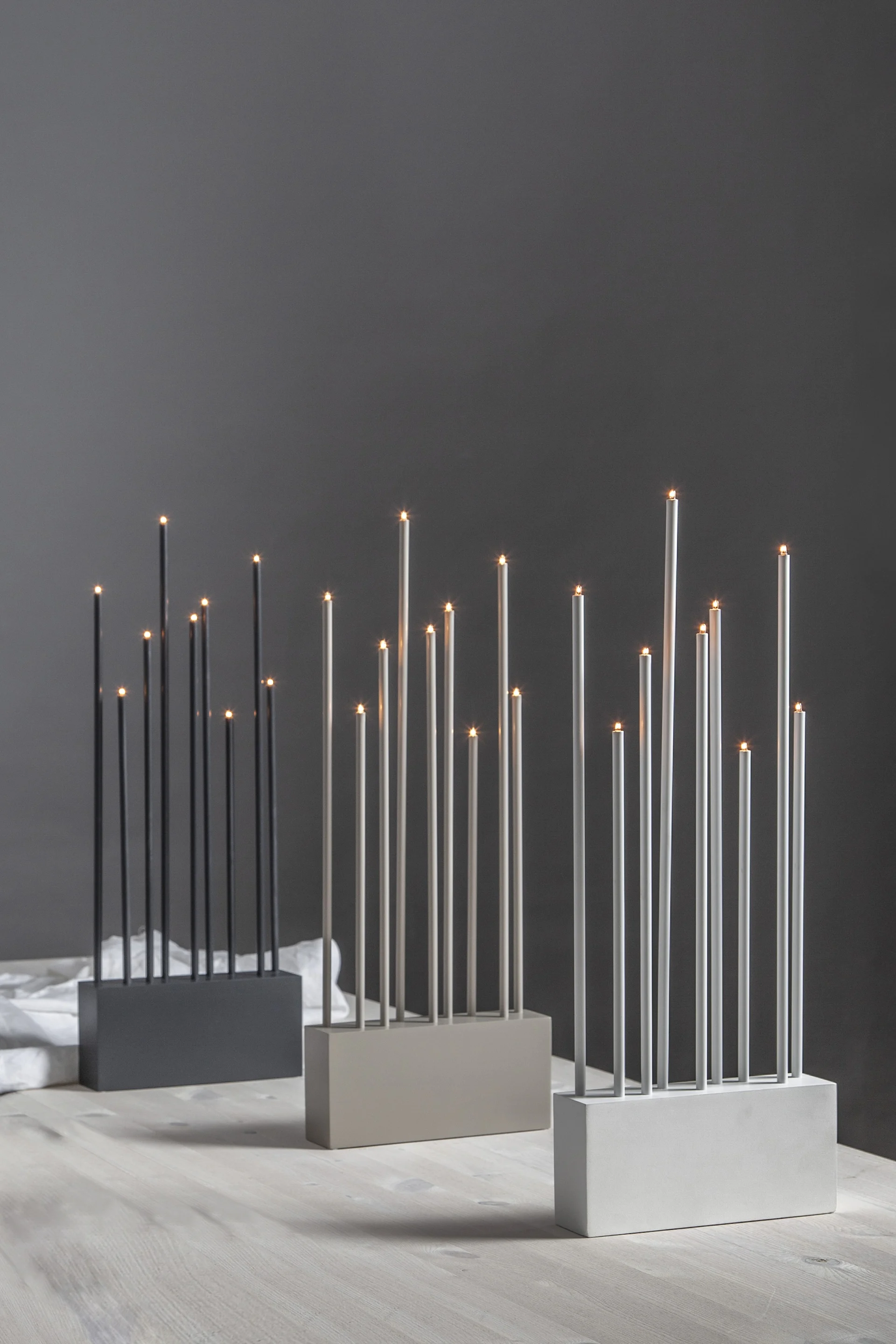 Moderne krom kandelaberlampe med fem glødende Edison-pærer på et trebord, med kongler og grå lin.