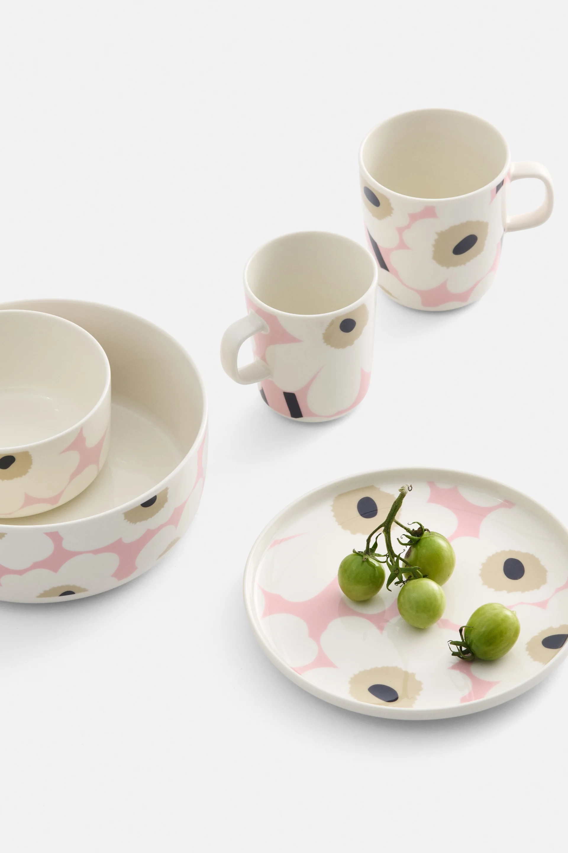 Kremfarget servise med rosa og svart blomstermønster, inkludert to skåler, to krus og en tallerken med grønne cherrytomater.