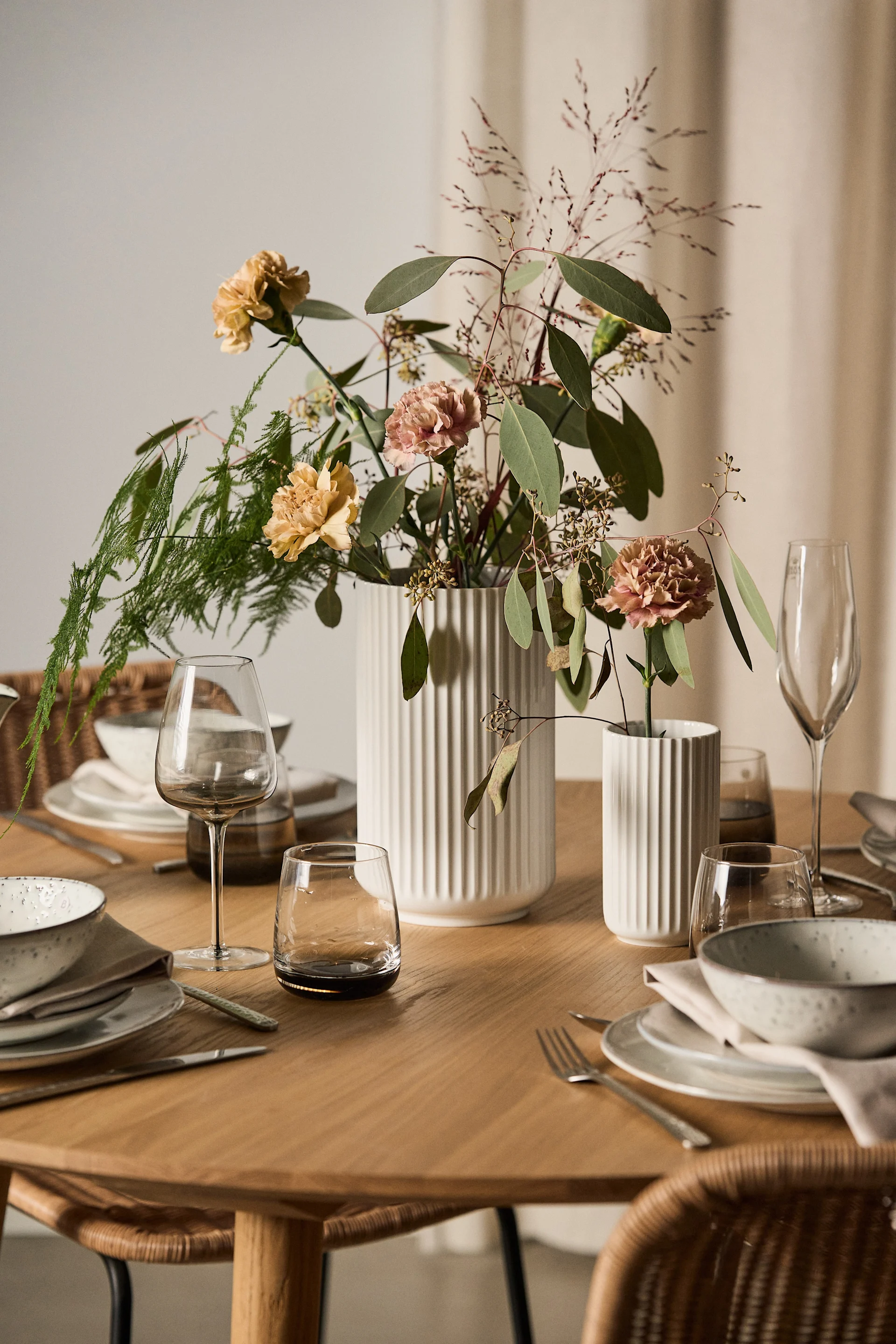 En fin gave til valentinsdag er blomster med en matchende vase. Her står to hvite vaser fra Lyngby Porcelæn med blomster på et dekket bord.