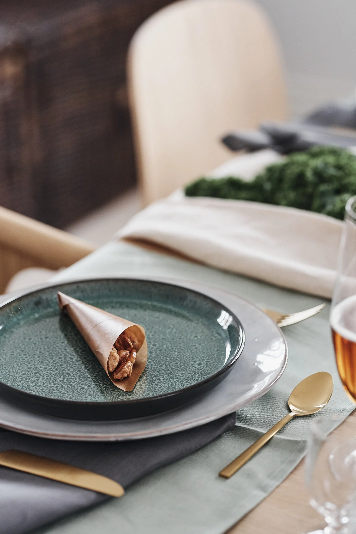 En papirkjegle med brente mandler som hviler på middagstallerkenen blir søt pynt på bordet.