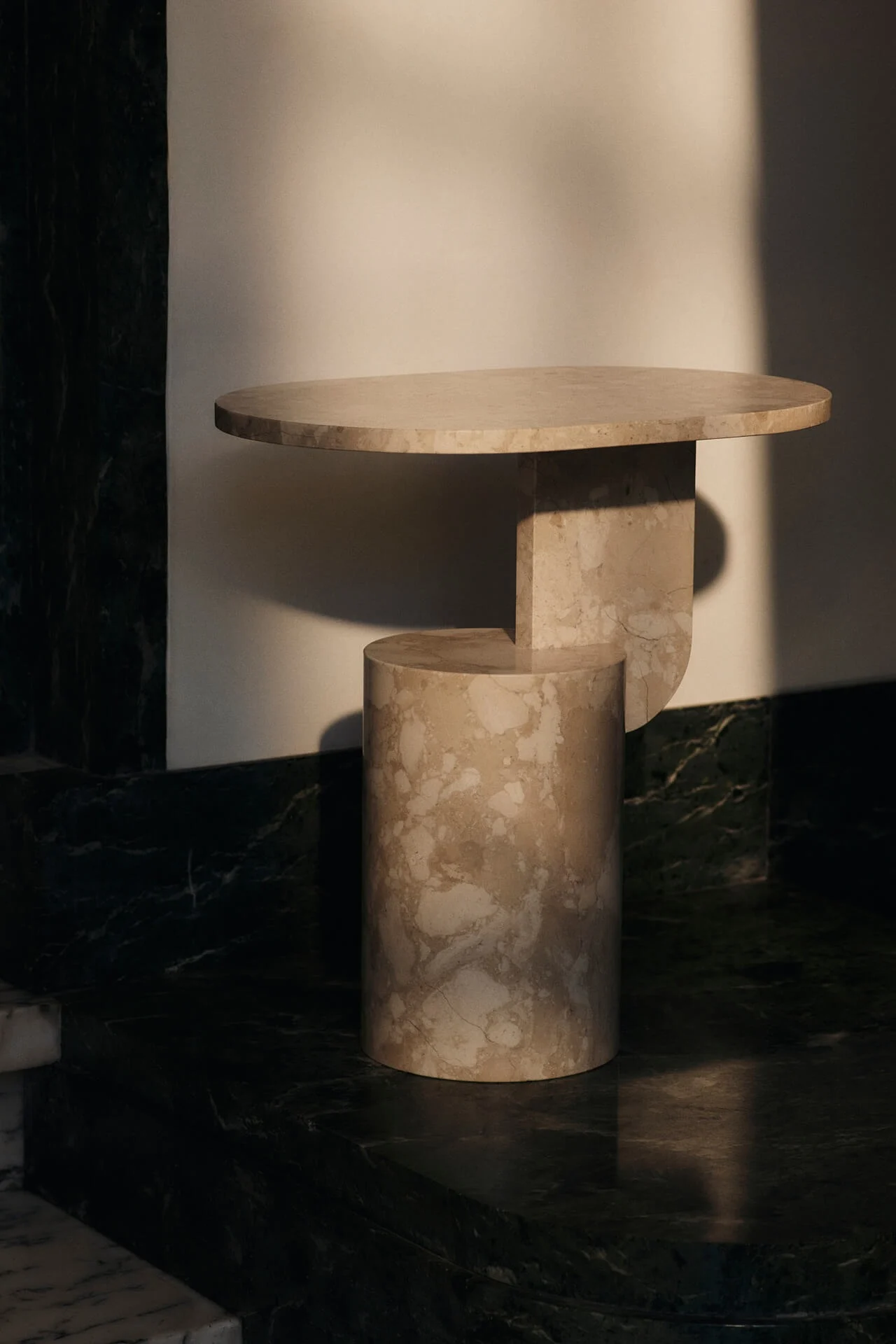 Moderne sidebord i beige marmor med rund plate og geometrisk base mot en lys vegg.