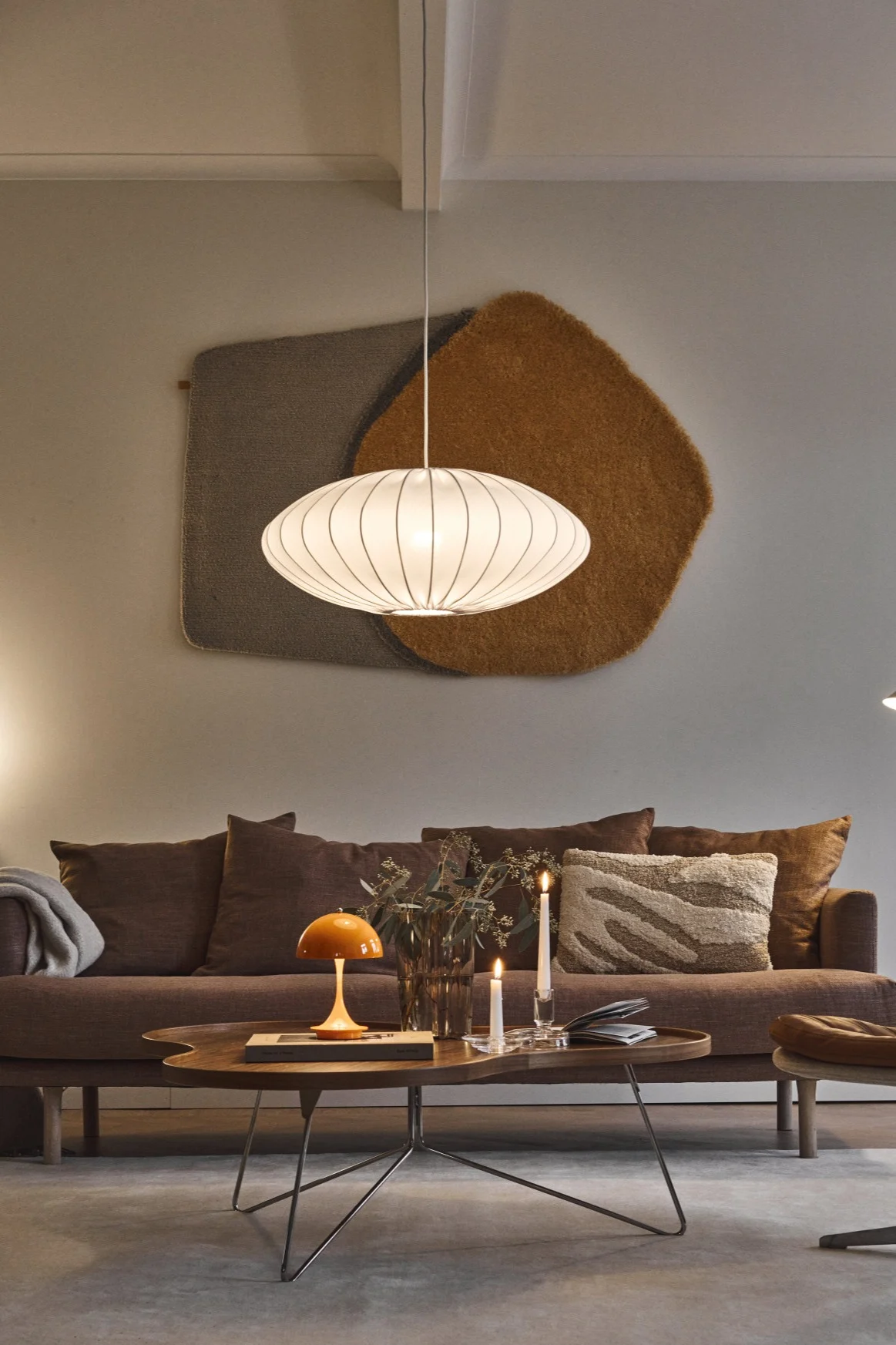 Koselig stue med brun sofa, salongbord, oransje sopplampe, lys, hvit pendellampe og brun skinnlenestol.