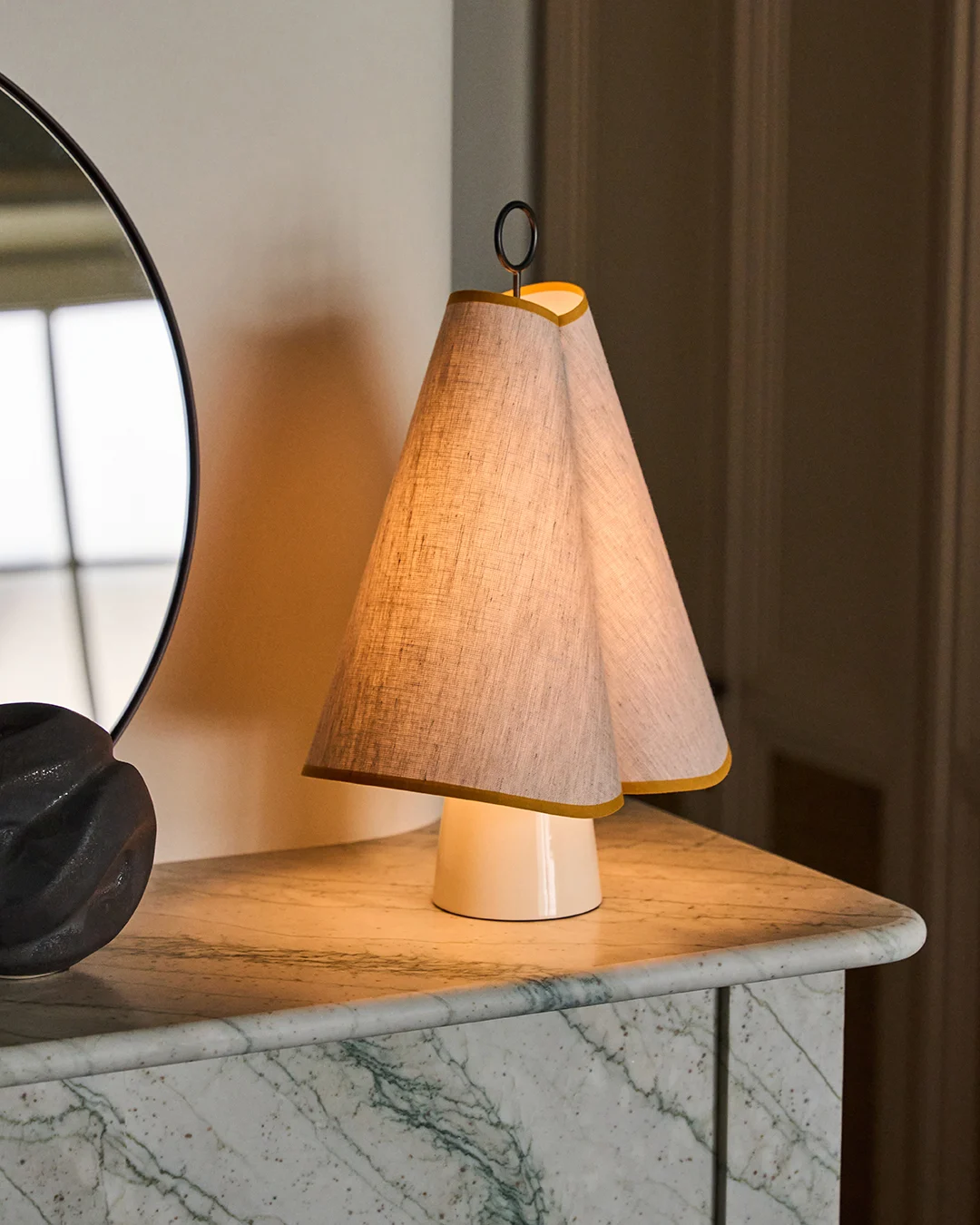 En unik bordlampe med dobbel konisk stoffskjerm trimmet i gult, som kaster et varmt lys på en grønn marmorplate.