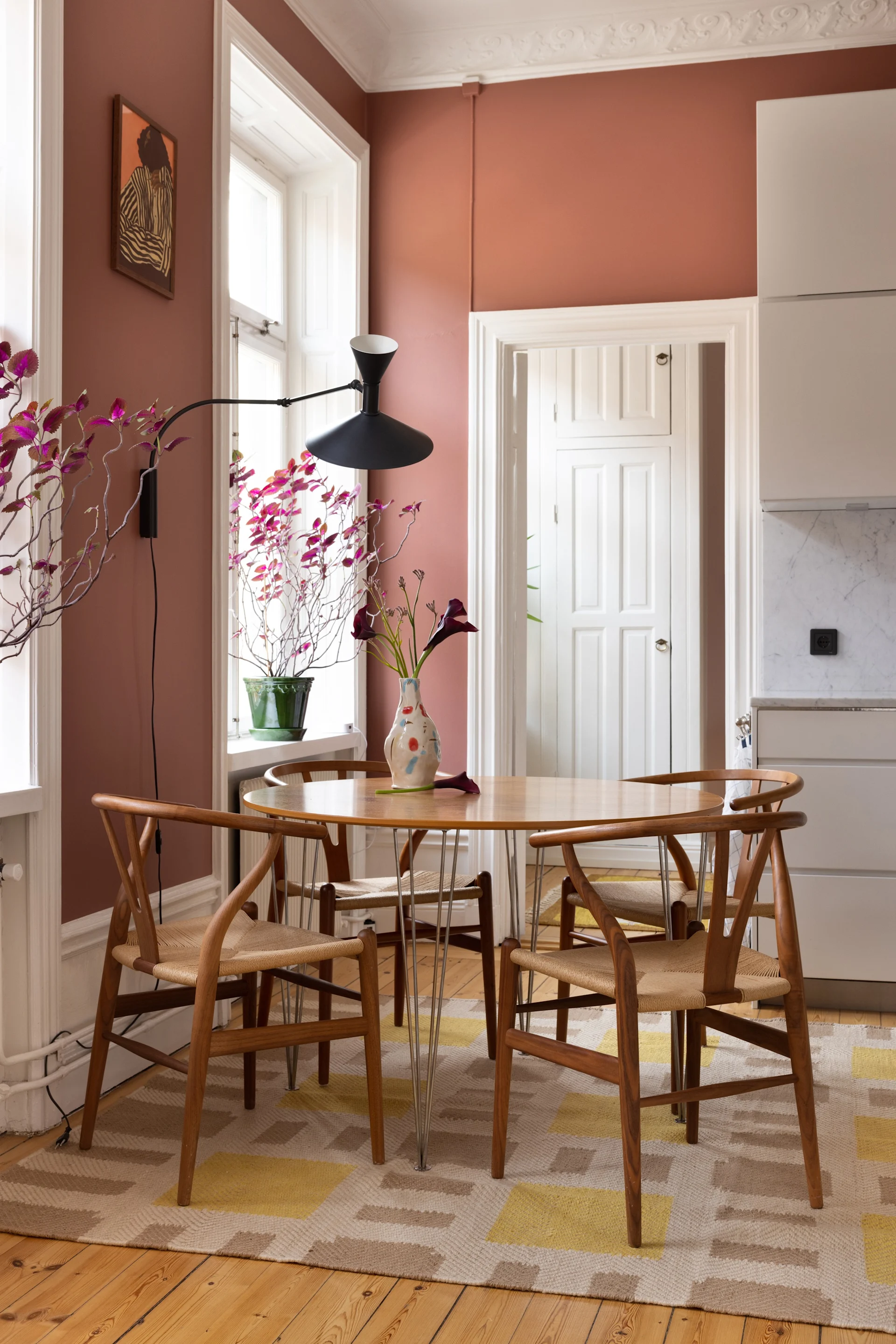 Gulvtepper til spisestuen: Evelina Kroon-juteteppet ligger i et fargerikt kjøkken under en spisegruppe med et rundt trebord og fire matchende stoler.