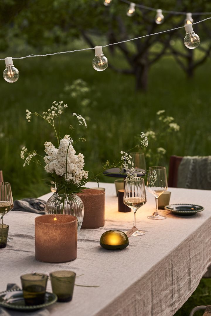 En borddekking til sommerfesten er ikke komplett uten bærbar belysning. Her ser du Soft Spot bærbar LED-lampe fra Rosendahl og Star Trading lysslynge.