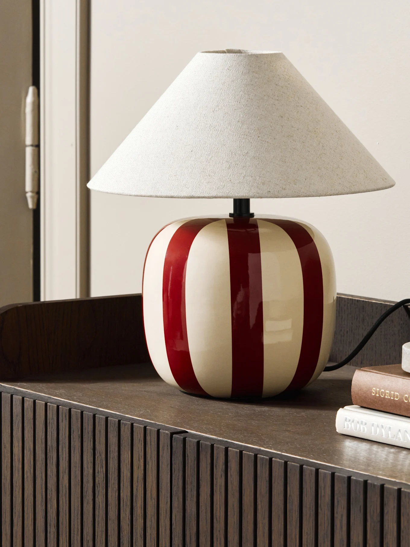 Lyseblå soppformet bordlampe på en rødbrun bok, på en bølget hylle.