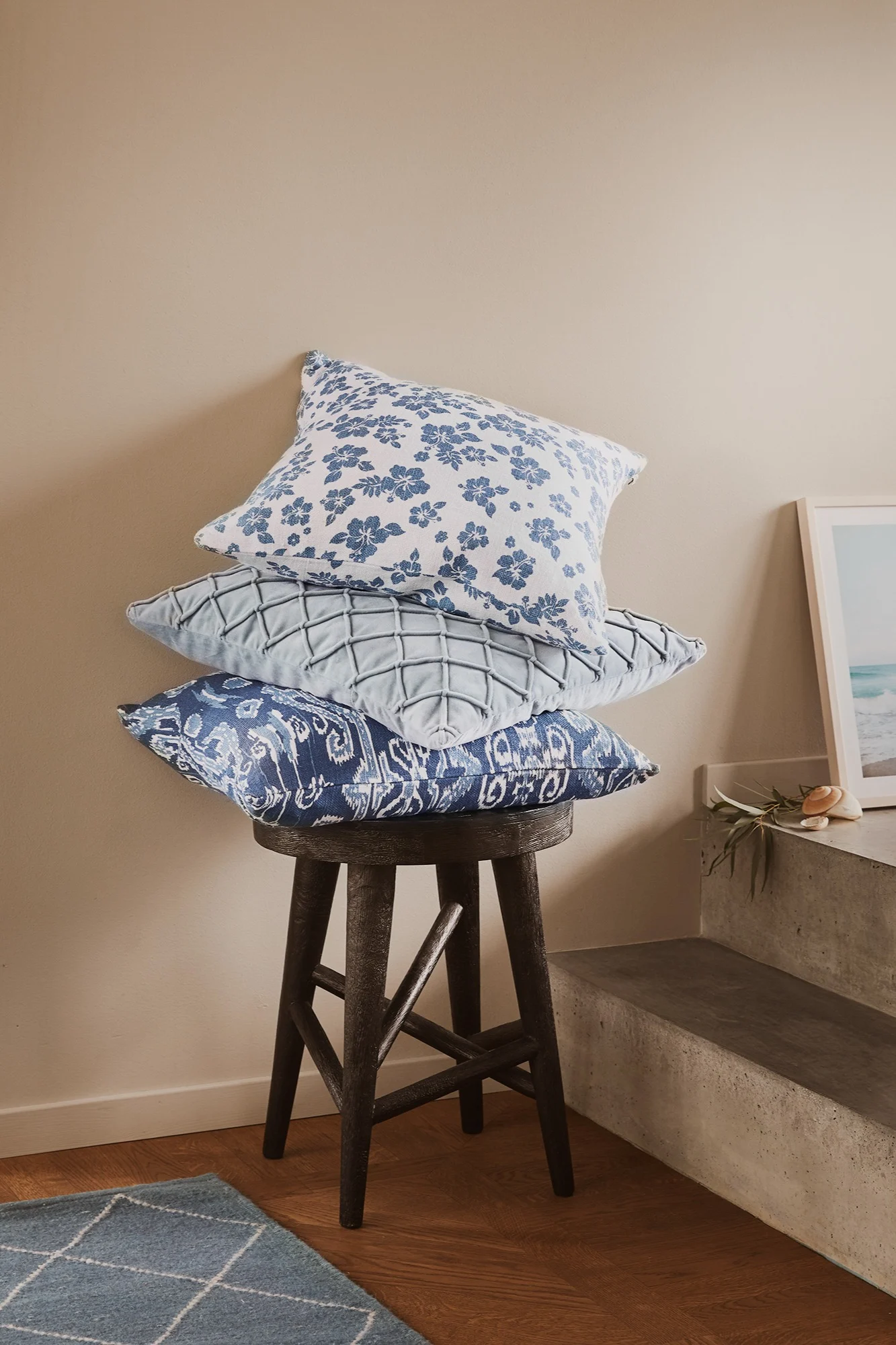 Putetrekk fra Chhatwal & Jonsson i tre forskjellige mønstre i blått er stablet på en stol i mørkt tre.