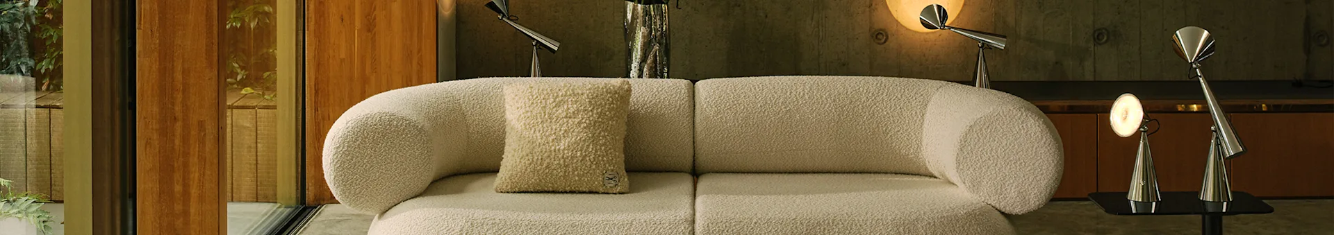 Moderne stue med en off-white bouclé modulsofa, et lyst mønstret teppe og metallamper.