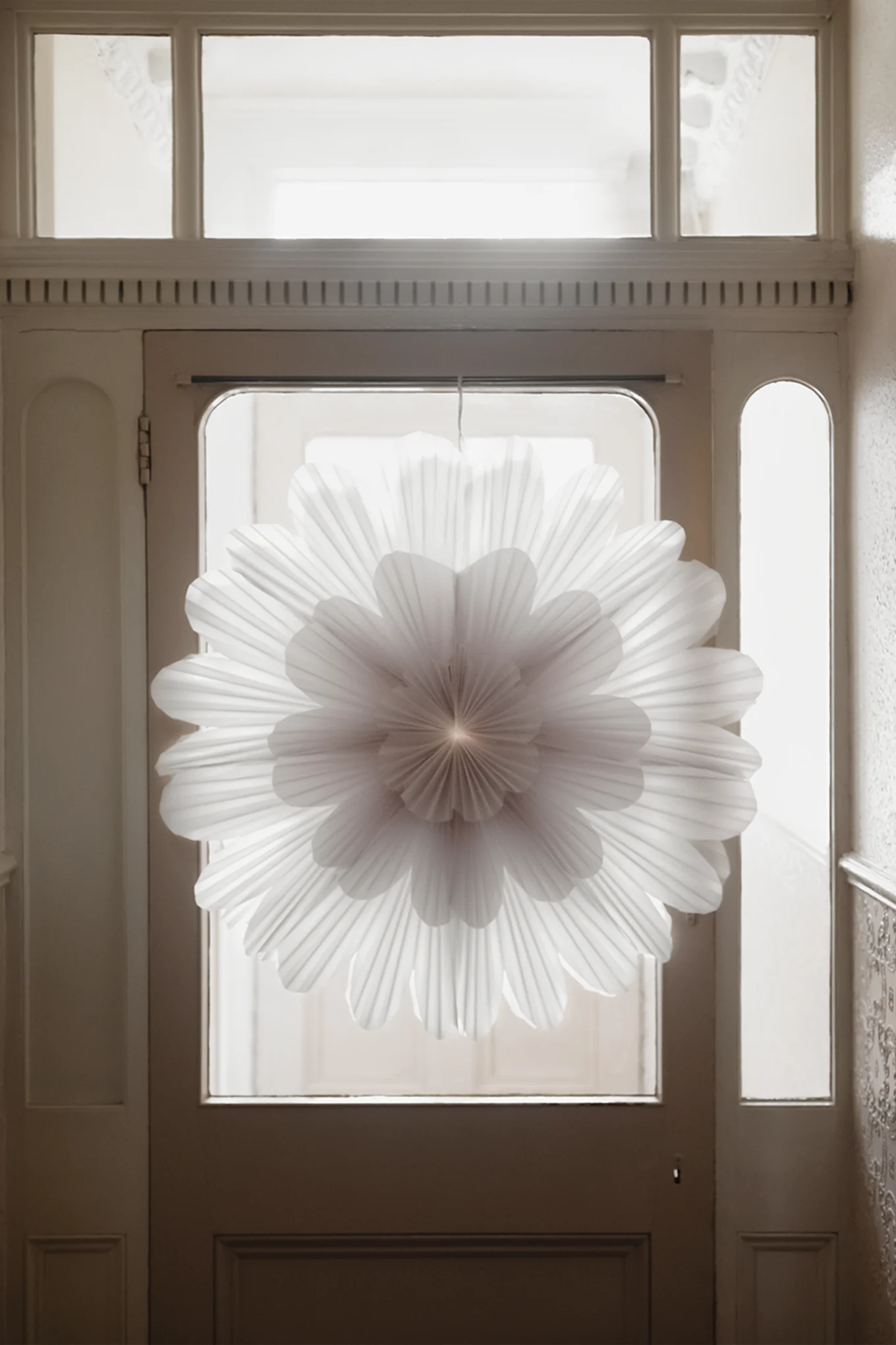 Minimalistisk julepynt– her ser du papirstjernen Snöblomma hengende i en døråpning med lys som skinner gjennom bakfra.