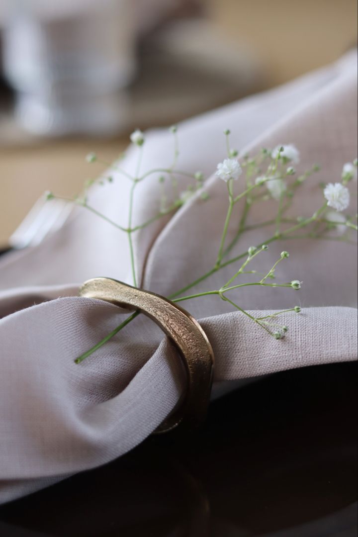 Hvordan brette servietter - nærbilde av en brettet serviett med en blomst og en serviettring i gull.