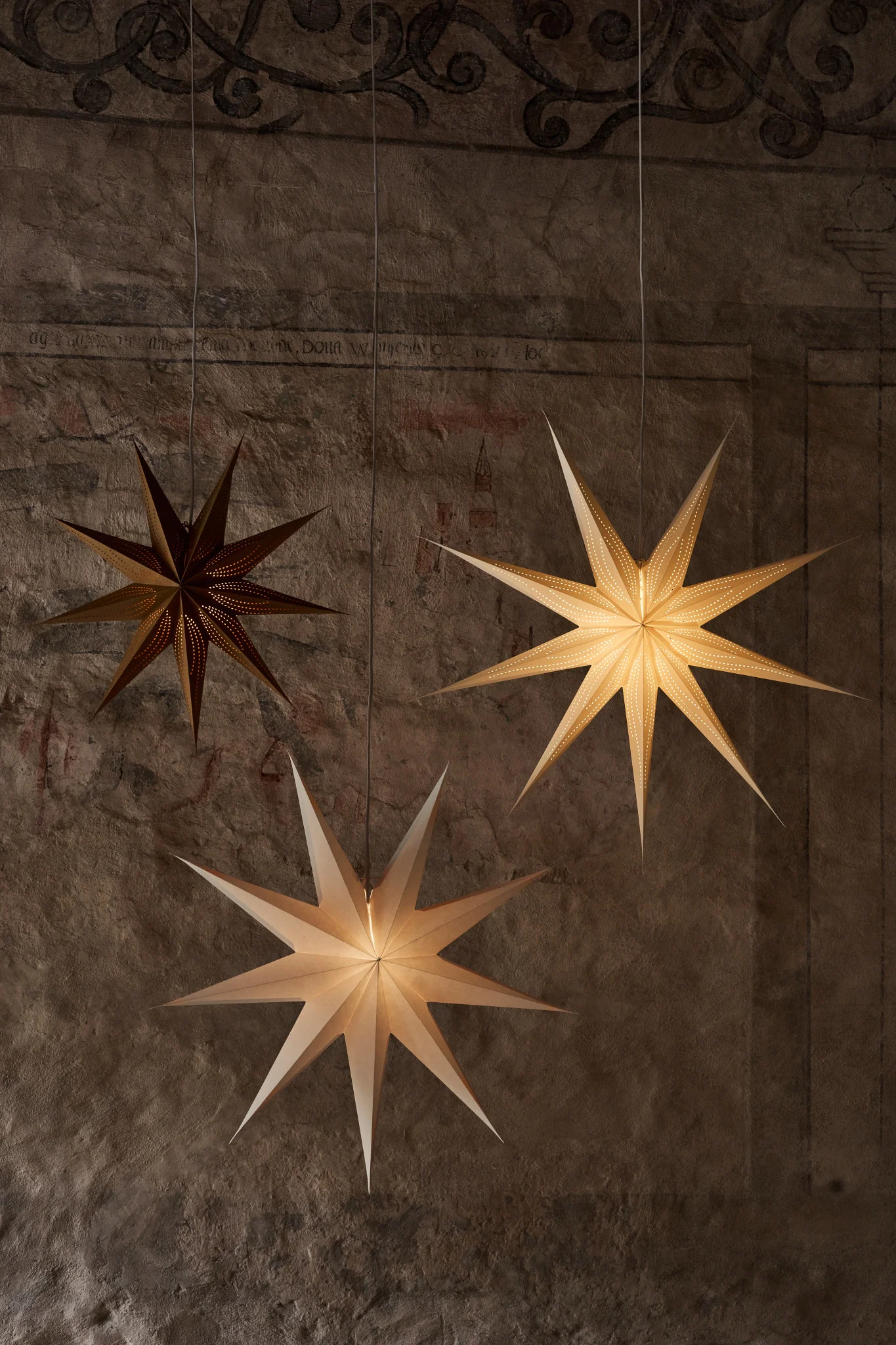 Venja, en adventsstjerne i papir fra Broste Copenhagen, henger i vinduet sammen med et par lysestaker og en vase.
