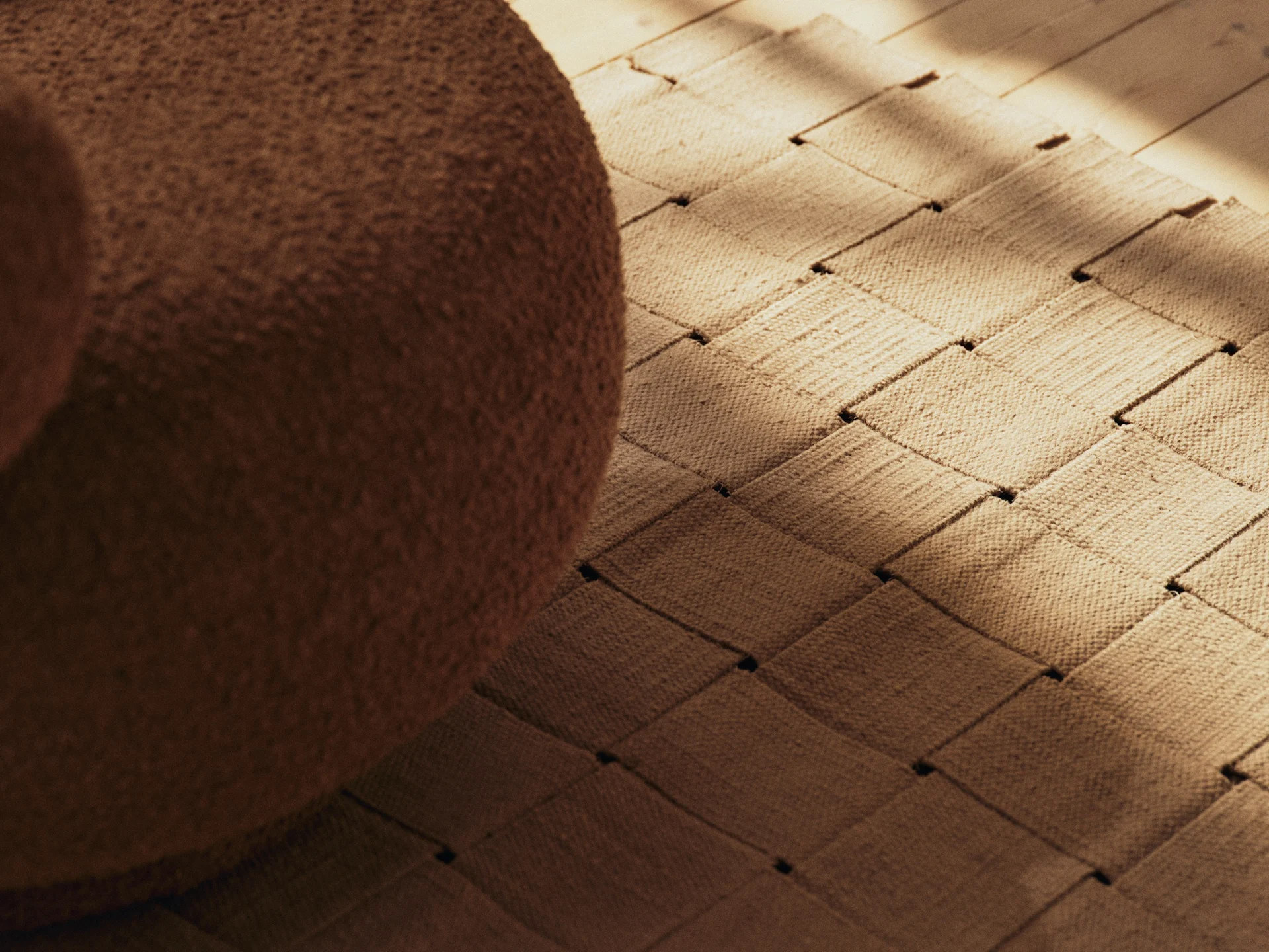 Brune bouclé-møbler, et vevd teppe og et tregulv med solbelyste skygger.