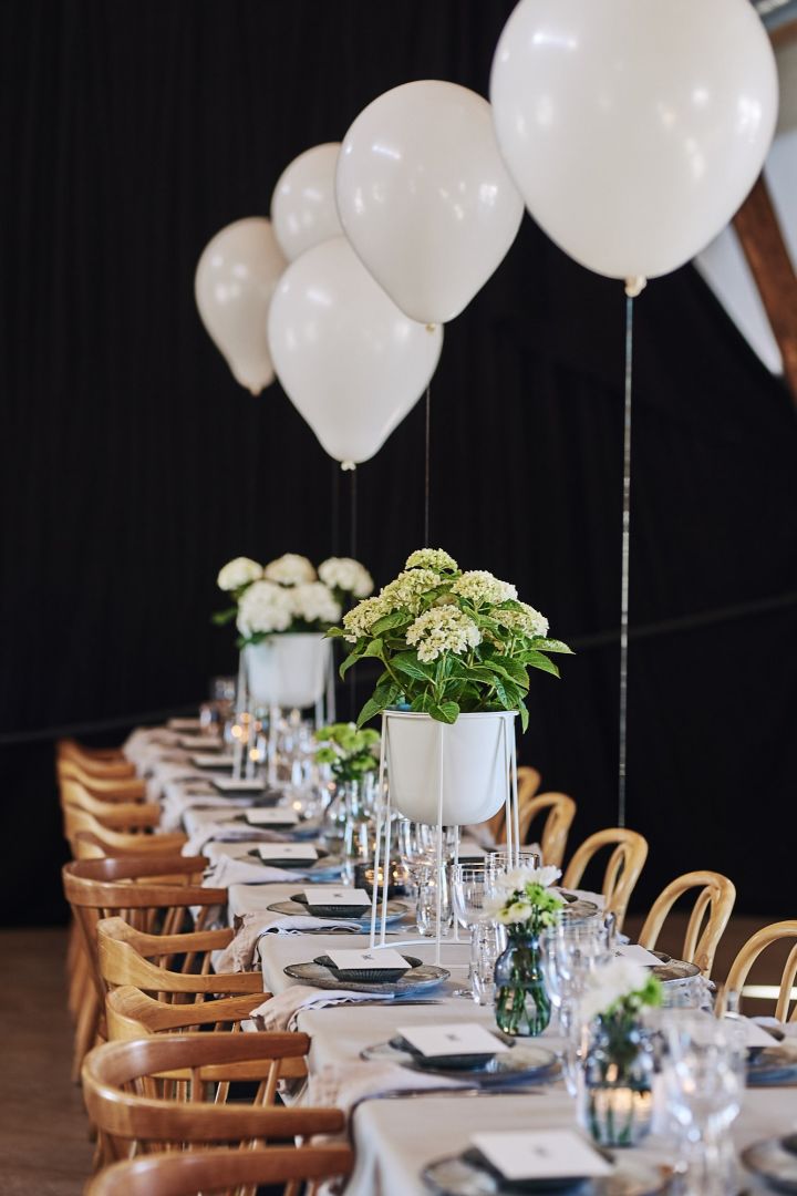 Et festbord i hvitt med ballonger og blomster som centerpiece.