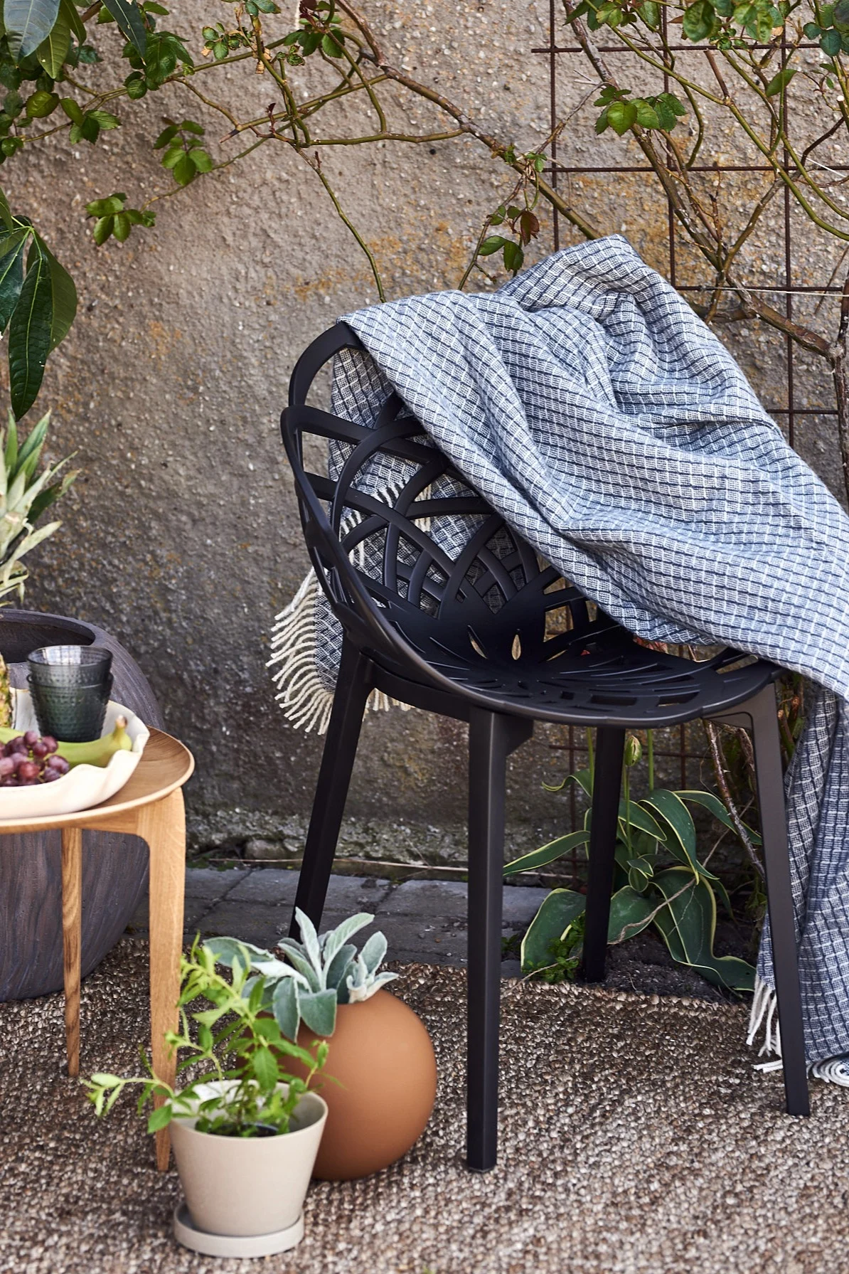 Blått ullpledd fra Nordic Nest på en sort utestol fra Muubs på en terrasse innredet i middelhavsstil.