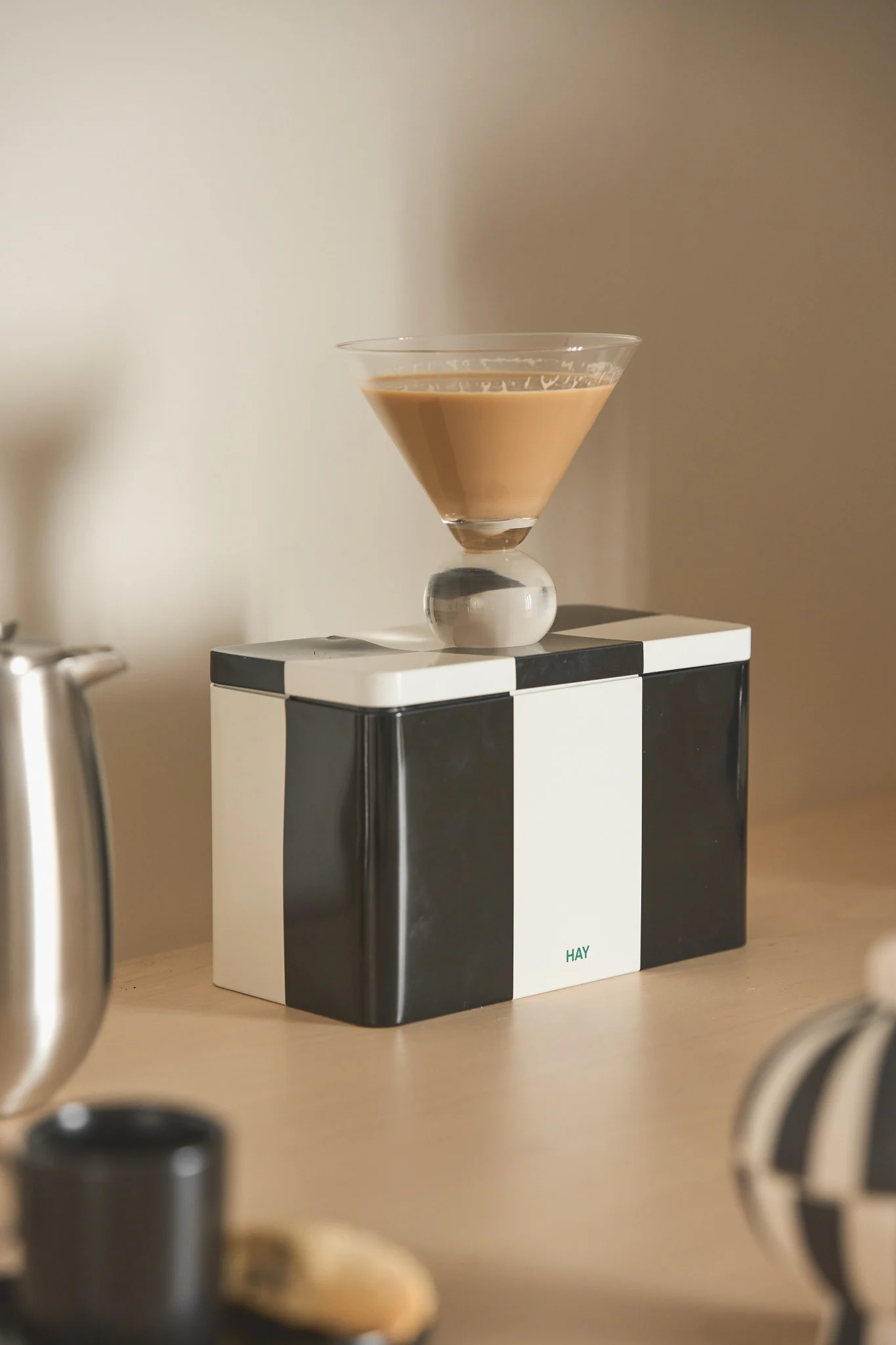 Martiniglass med lys brun drikke og sfærisk stett på en svart- og hvitrutete boks med 'HAY'-logo.