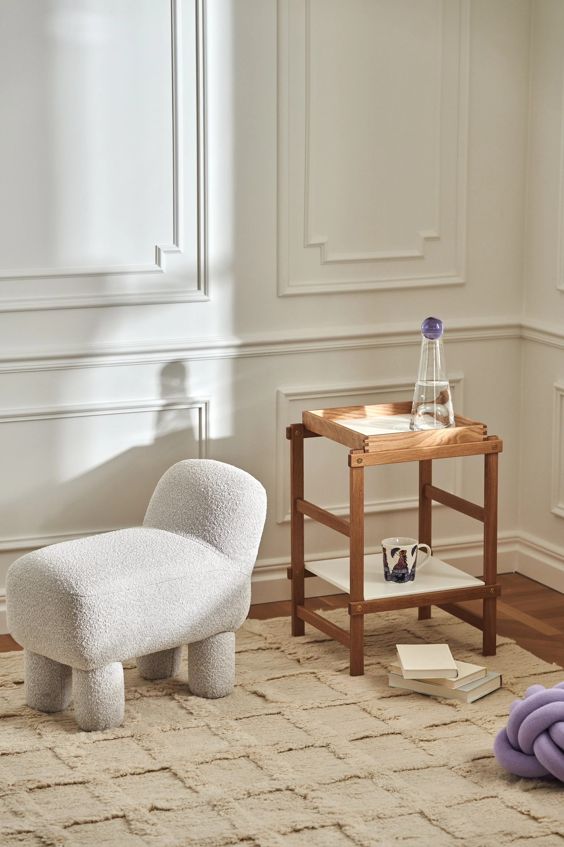 Stilren stue med produkter fra Design House Stockholm i form av Lulu-puff, Frame-hylle i eik, Knot-pute i lavendel og Elsa Beskow-krus.