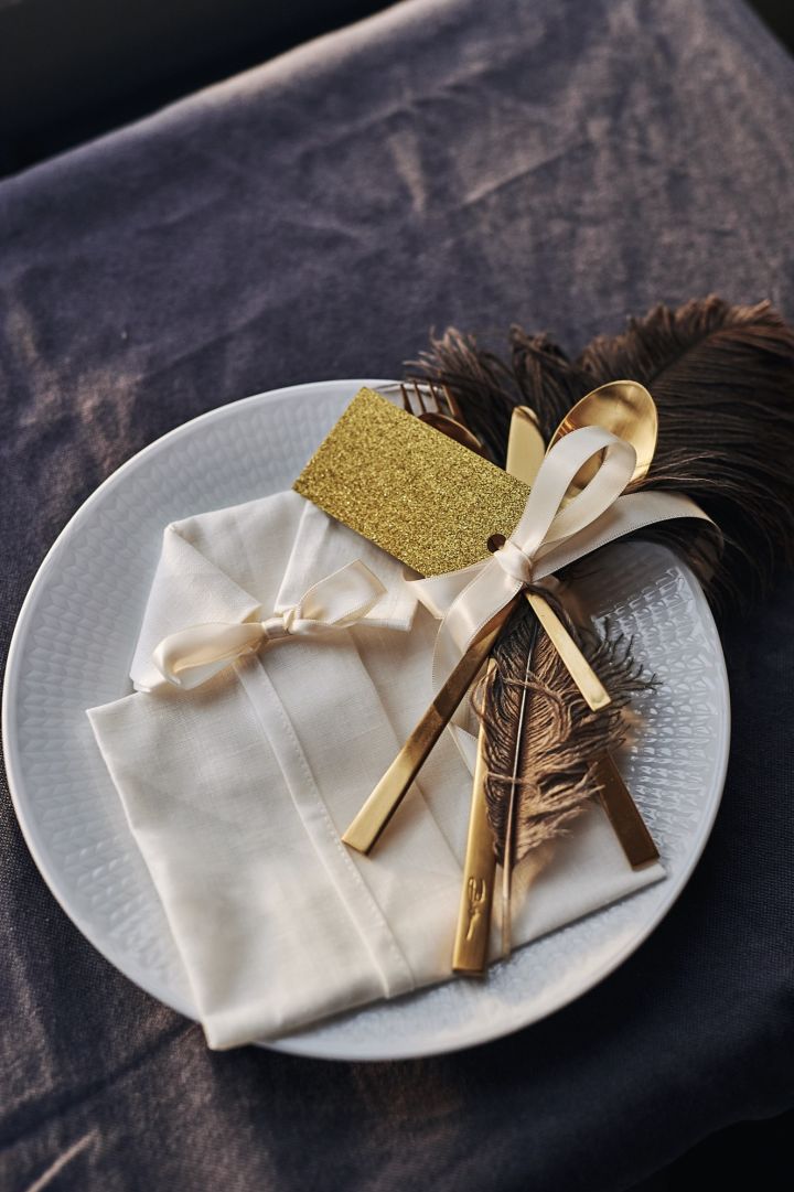 En brettet serviett i form av en skjorte til nyttår, jul, konfirmasjon eller fest ligger på tallerkenen med bestikk, bordkort og en dekorativ fjær.