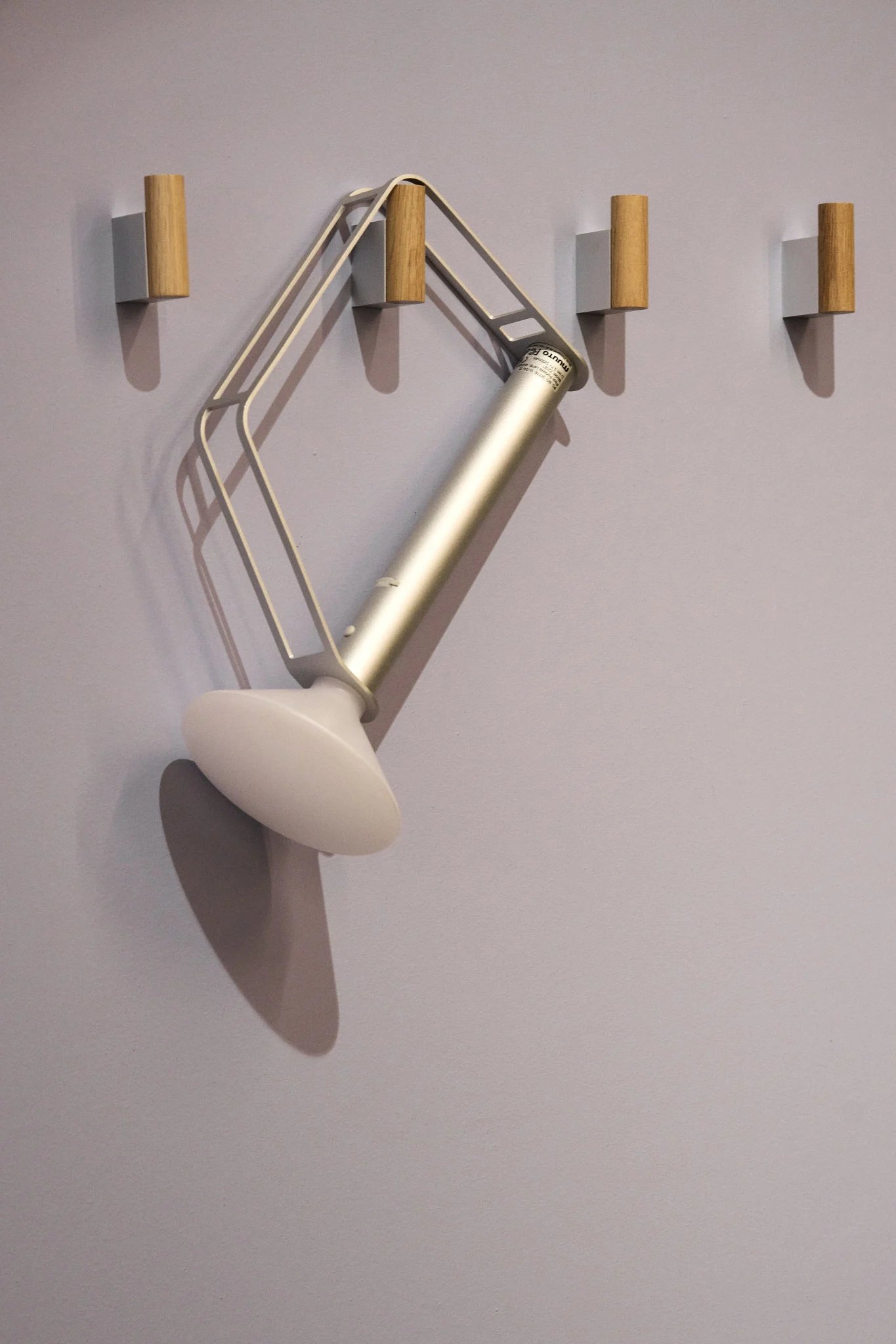 Den sølvfargede, bærbare Piton-bordlampen fra Muuto henger på én av fire kroker på veggen.