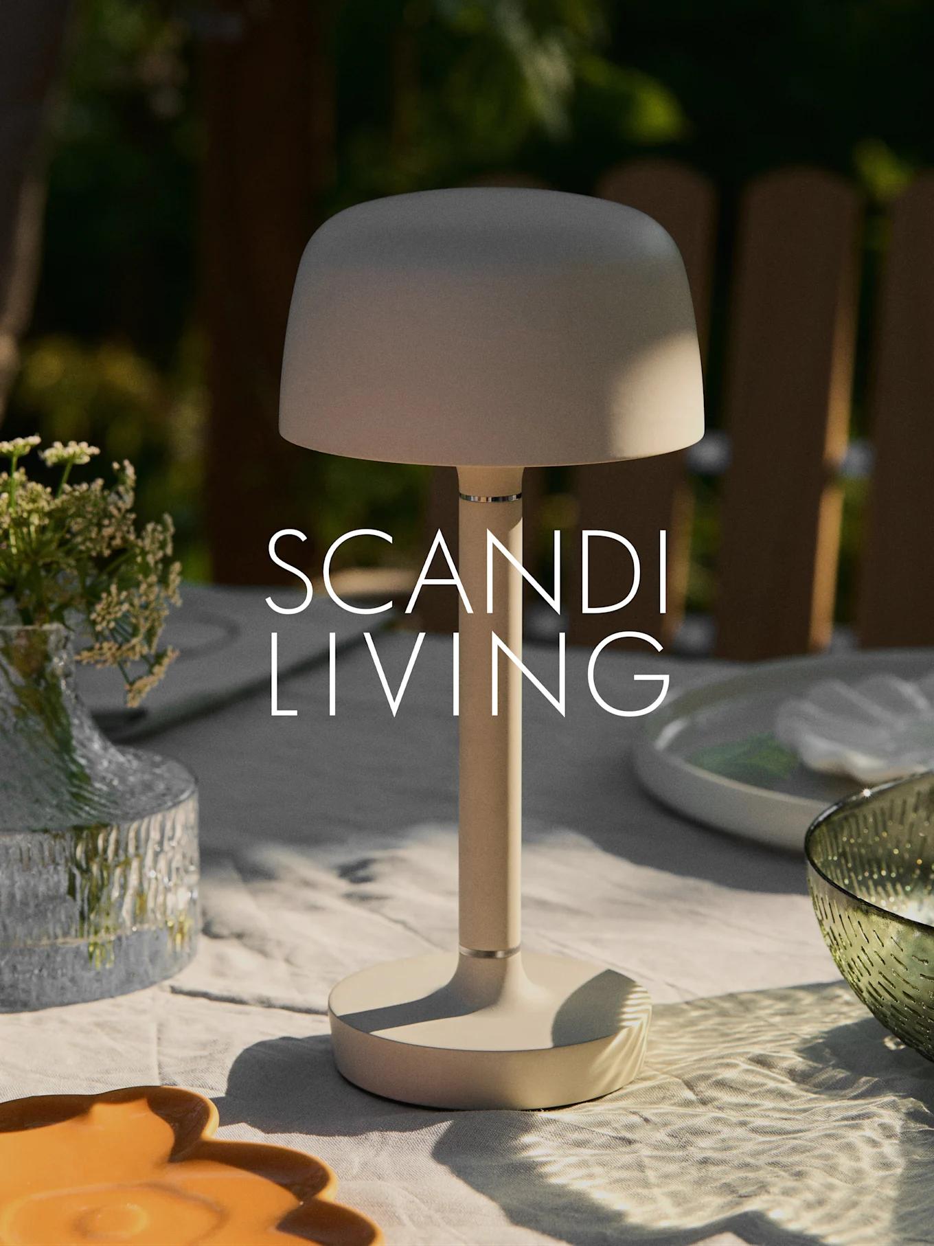 En beige moderne bærbar bordlampe på et utendørs bord med en vase med blomster og fat. Teksten "SCANDI LIVING".