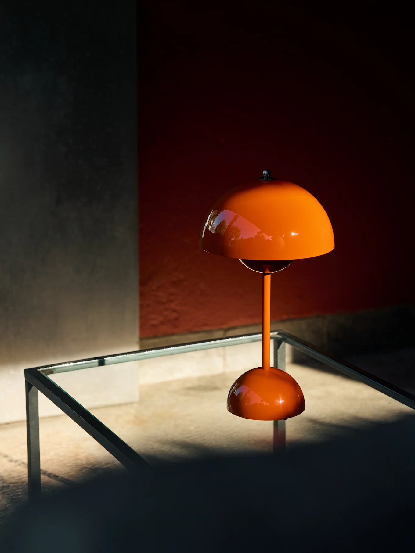 Oransje soppformet bordlampe på et glassbord, som reflekterer grøntområder.