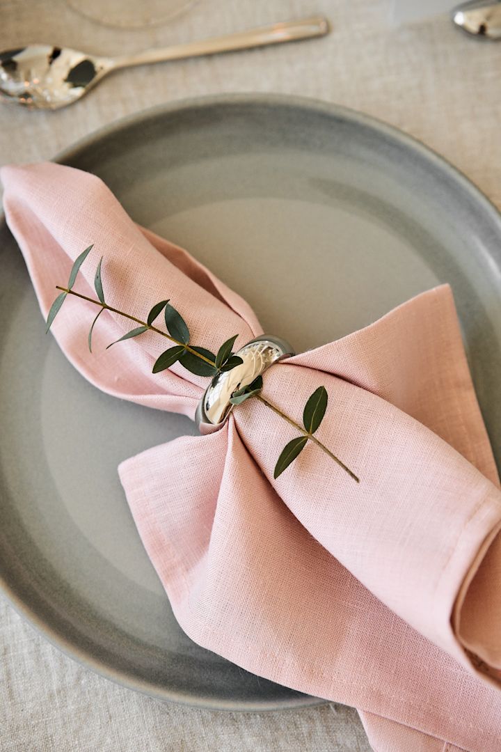 Dekorer bordet i myke toner til din romantiske middag hjemme. Her ser du Clean-servietten i Dusty Rose fra Scandi Living, festet med en serviettring og lagt på en tallerken.