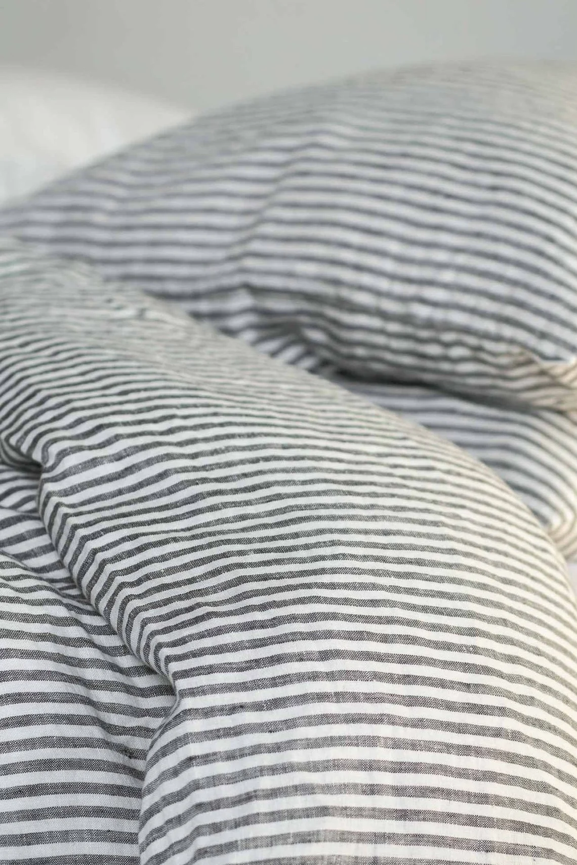 Nærbilde av en rufsete seng med svart- og hvitstripet sengetøy i lin.