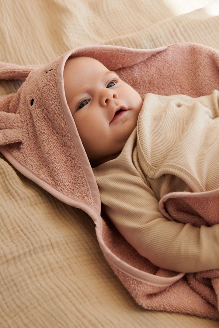 En baby ligger på et håndkle med hette i en matchende baby dress fra Garbo&Friends - perfekte gaveidéer til babyshower.