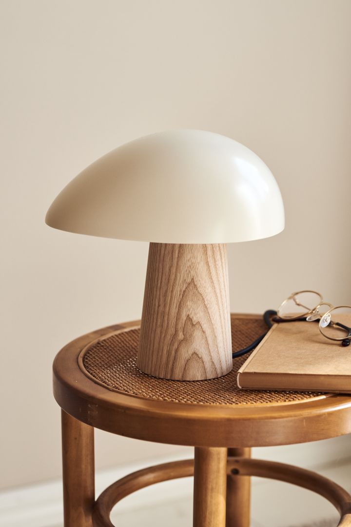 Forny hjemmet ditt med moderne bordbelysning - her ser du Fritz Hansen Night Owl bordlampe i hvitt og lyst tre på en krakk av rotting.
