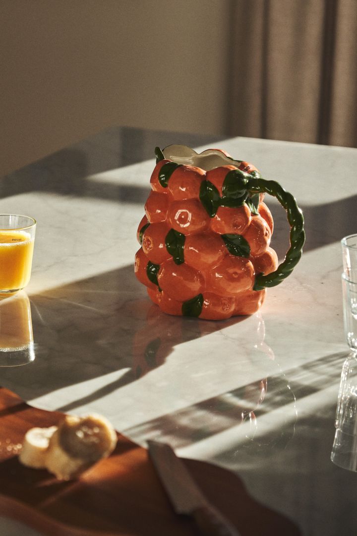 Mugge i svulmende form i oransje og grønt med mandariner som inspirasjon på et frokostbord, helt rett når man følger interiørtrender 2024.