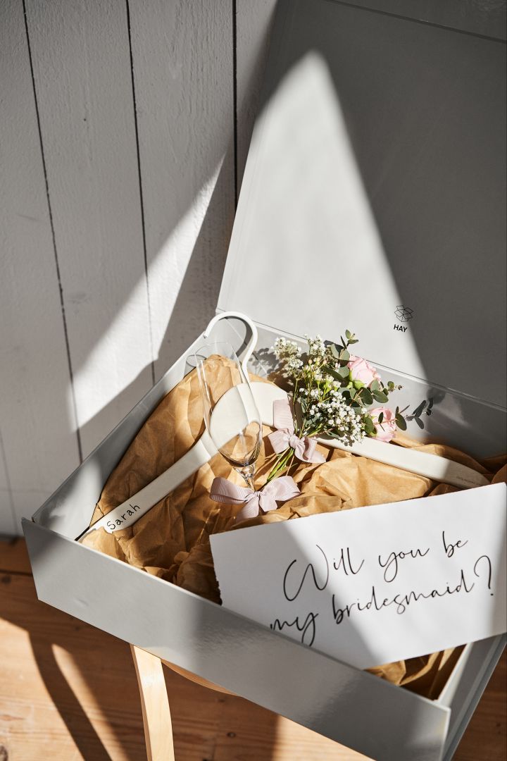 Bli inspirert av disse unike bryllupsideene som et personlig brudepikeforslag i en grå oppbevaringsboks fra HAY med en personlig kleshenger til kjolen og et champagneglass for å feire. 