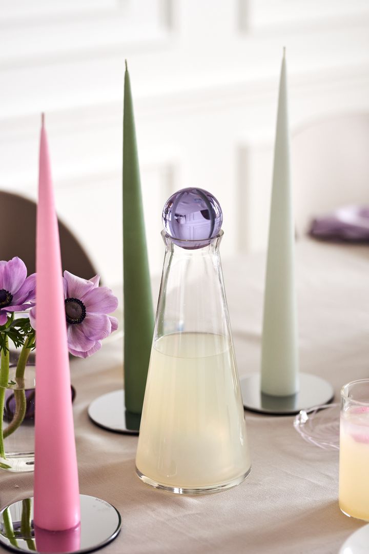 Dekk et festlig påskebord i vårlige pastellfarger med karaffelen Fia fra Design House Stockholm, som har en lyslilla glasspropp.