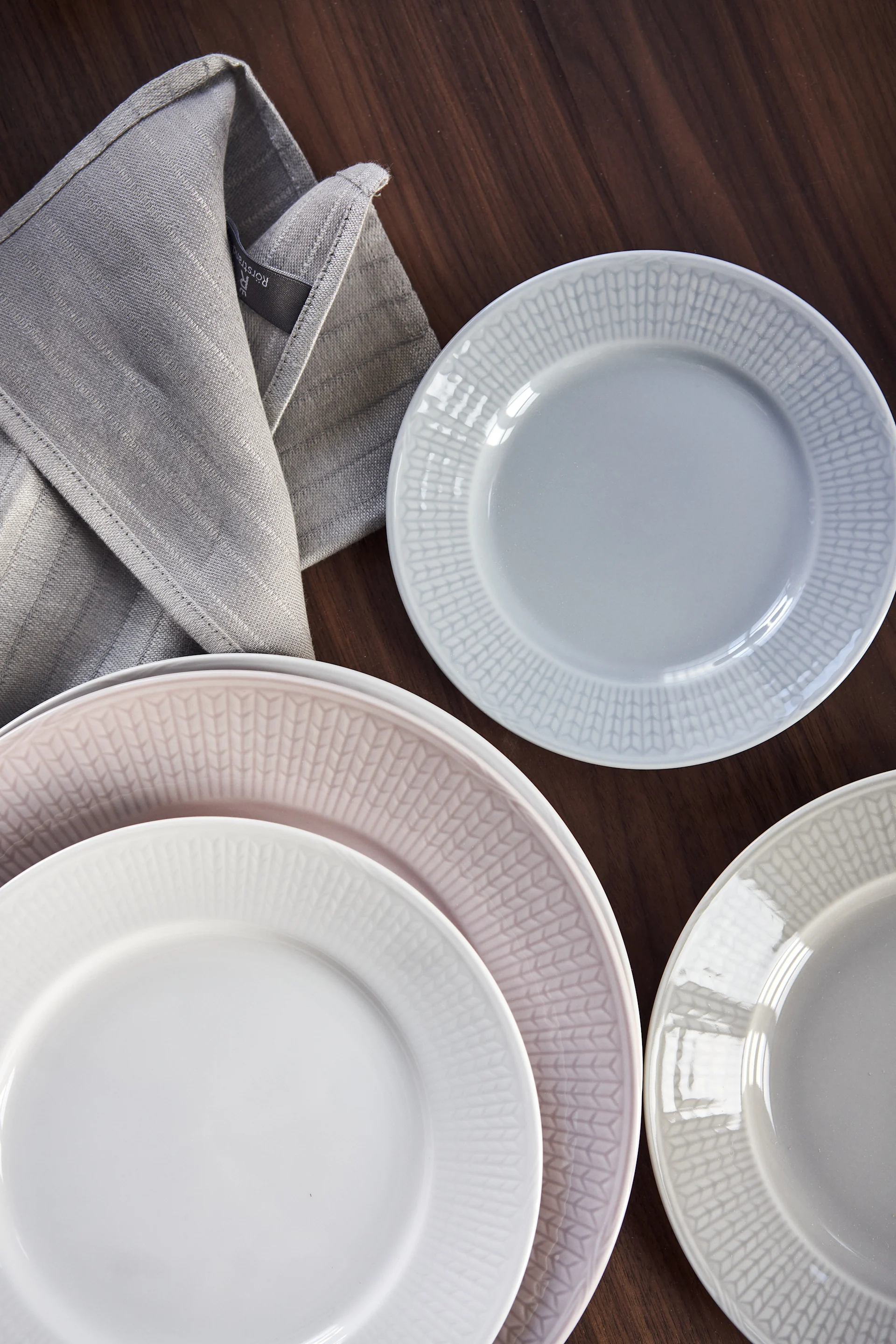 Swedish Grace tallerken i hvitt, rosa, blått og grått på et mørkt trebord.