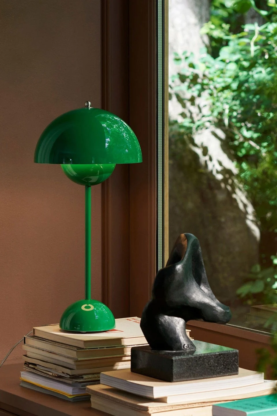 I en vinduskarm står Flowerpot bordlampe i signalgrønn fra &Tradition, designet av Verner Panton, oppå en stabel med bøker.
