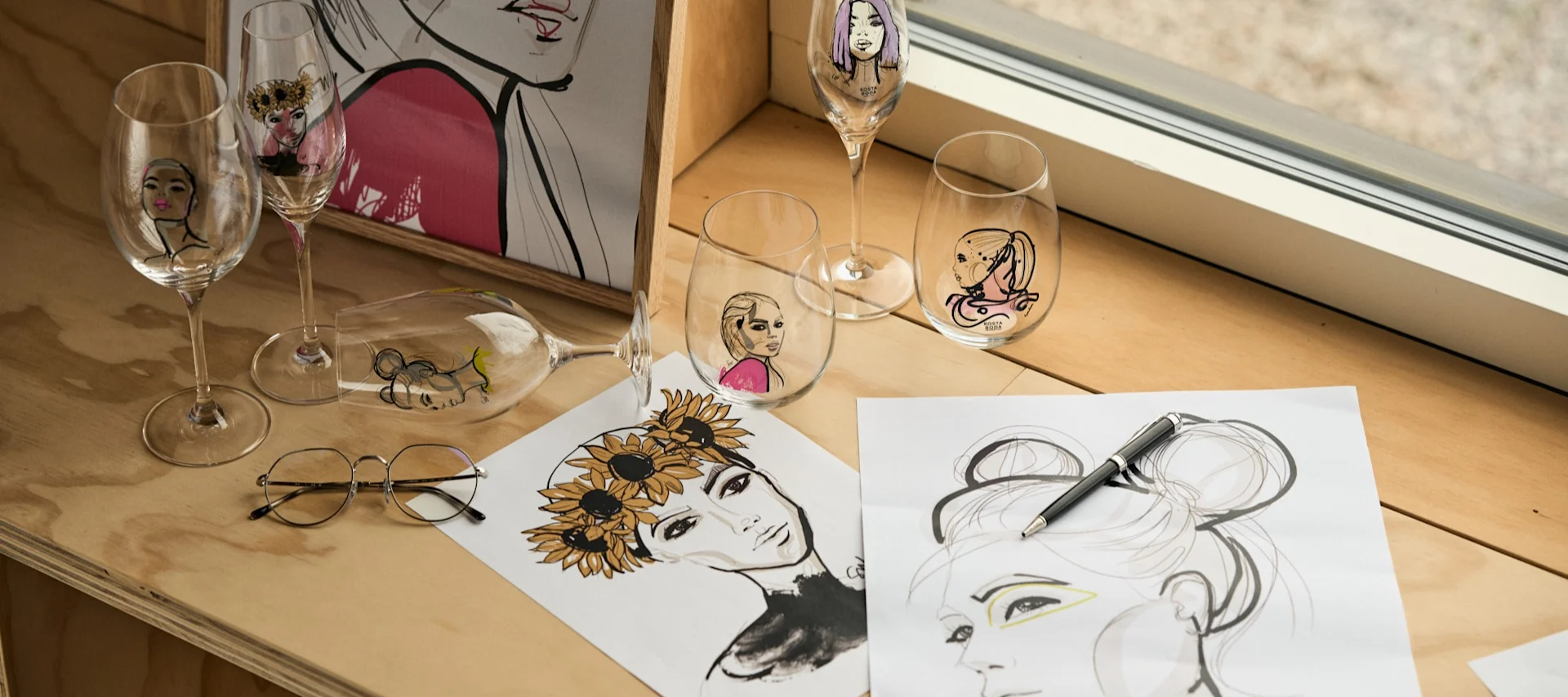 All About You-serien, designet av Sara Woodrow for Kosta Boda, kolleksjonen med glass samlet i et vindu på en kryssfinerbenk.