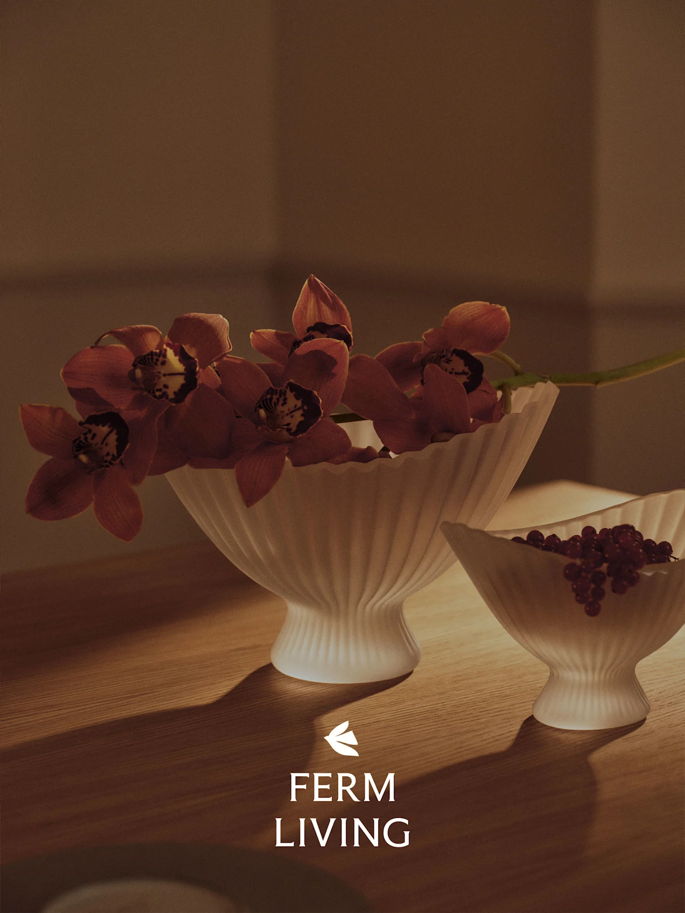 To rillede hvite skåler på et trebord, den ene med røde orkideer, den andre med røde bær, i varmt lys.