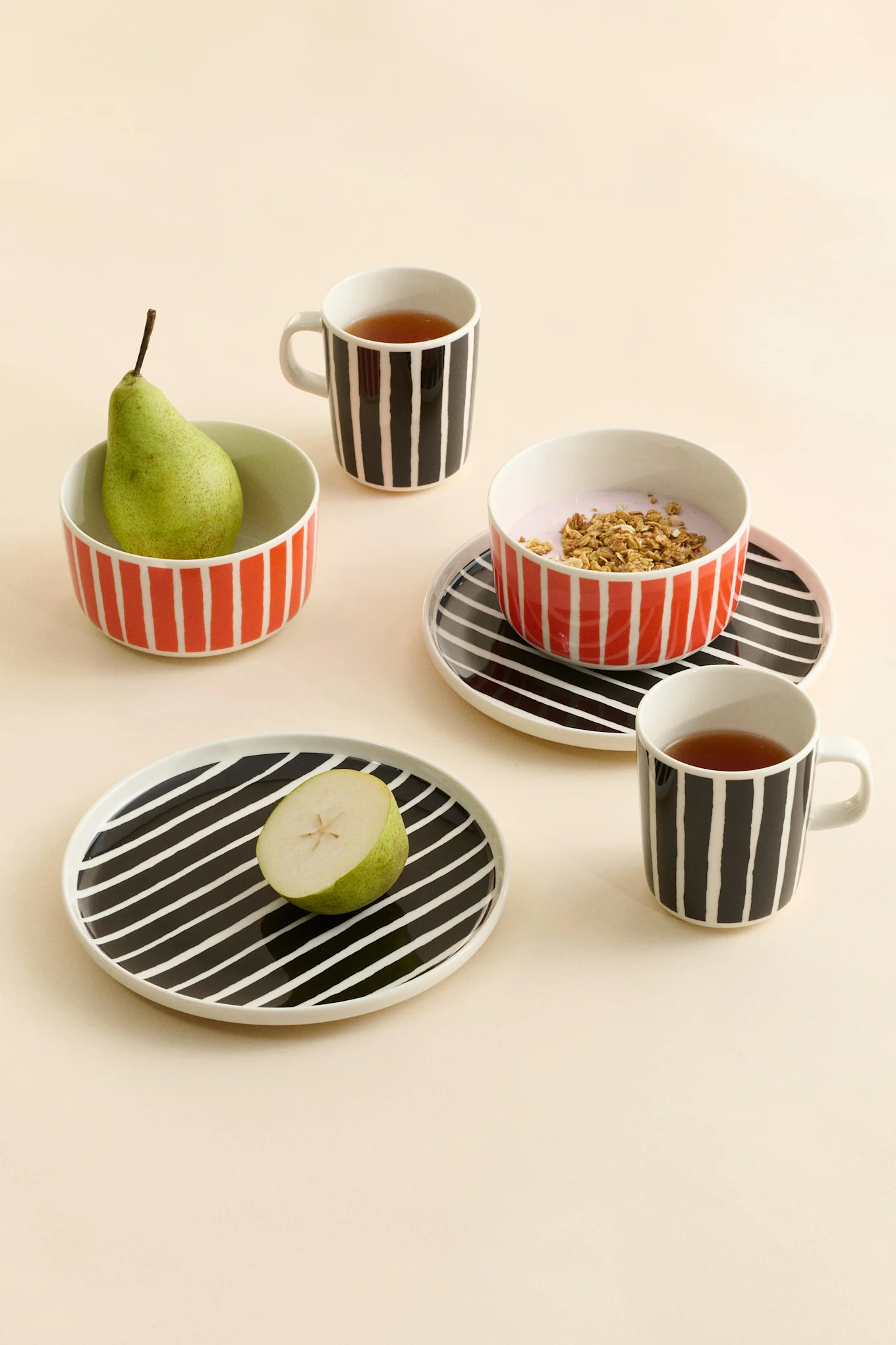 Stripete keramikkrus med te, skåler med en pære og yoghurt med granola, og tallerkener med en halv pære.