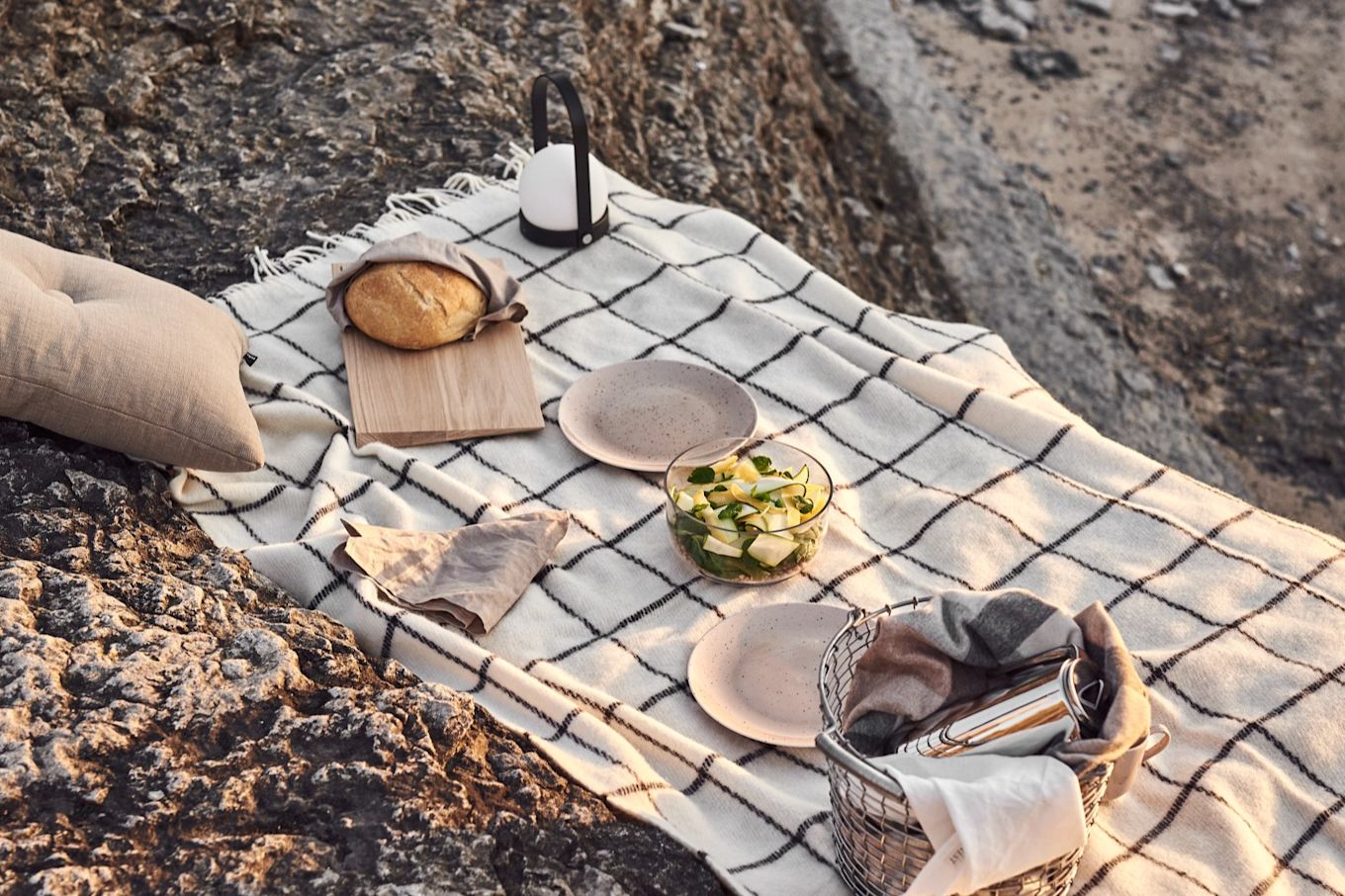 Nyt en piknik på stranden ved solnedgang med diverse snacks, pledd og oppladbare lampe - her Carrie-lampen i sort fra Menu.