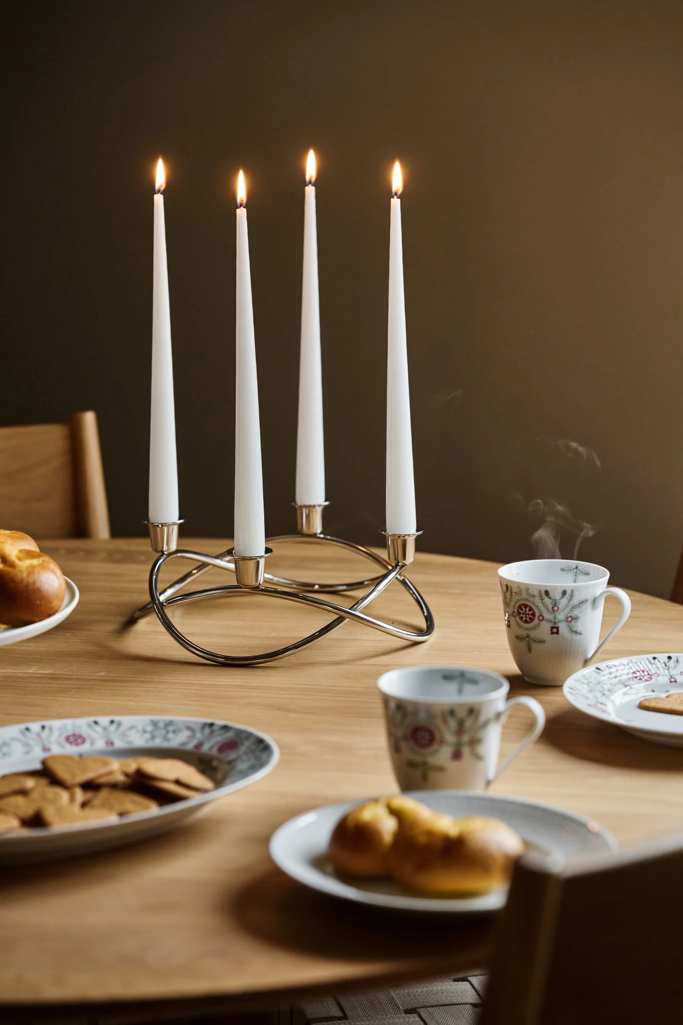 Adventslysestaken Season står på et julebord med pepperkaker og lussekatter.