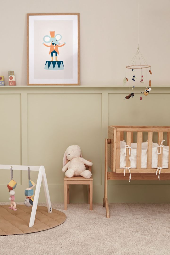 Et bilde av et babyrom med en mobil hengende over en sprinkelseng og et gulvgym på gulvet. Mobiler er perfekte gaveidéer til babyshower.