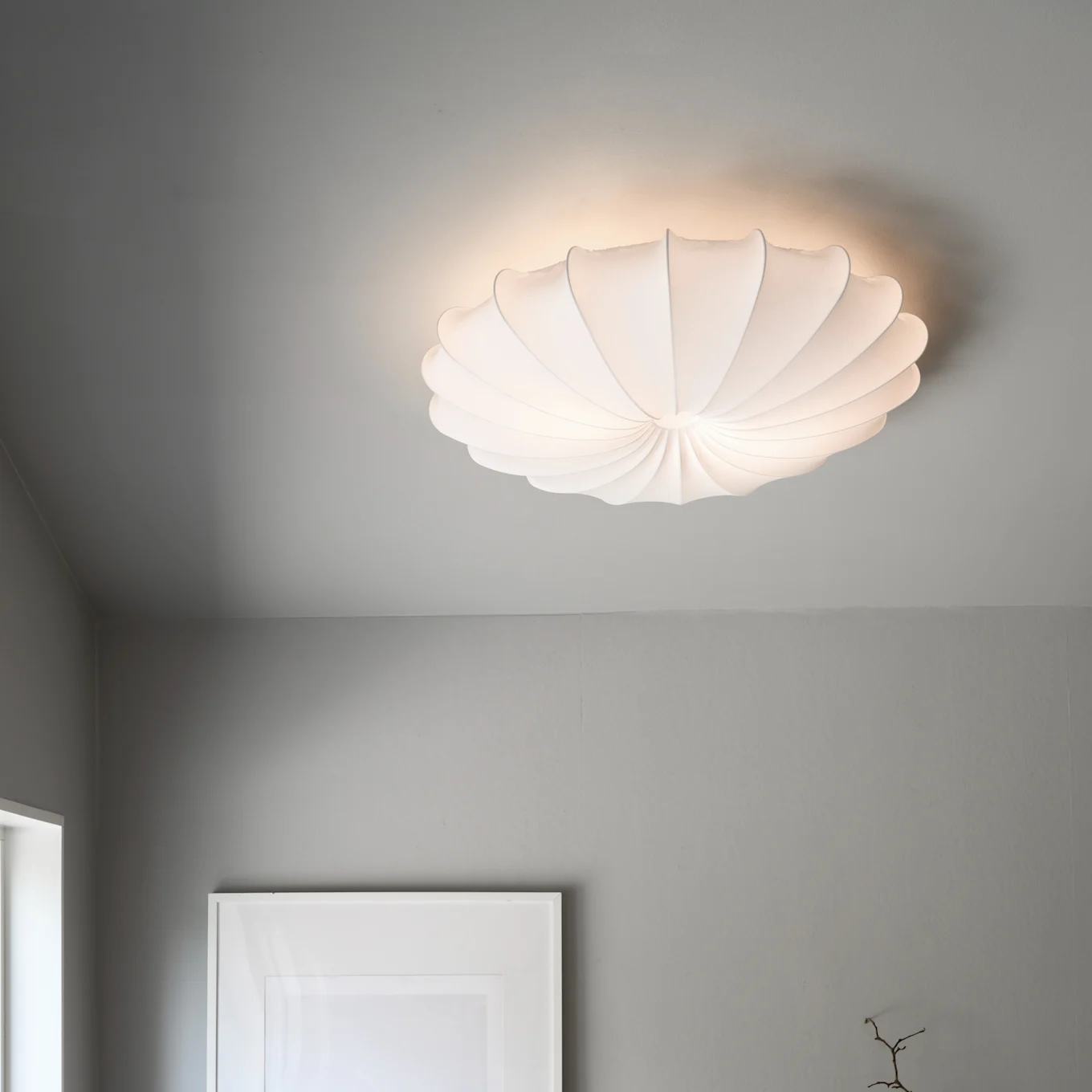 En hvit, plissert, skjellformet taklampe lyser opp et grått tak.