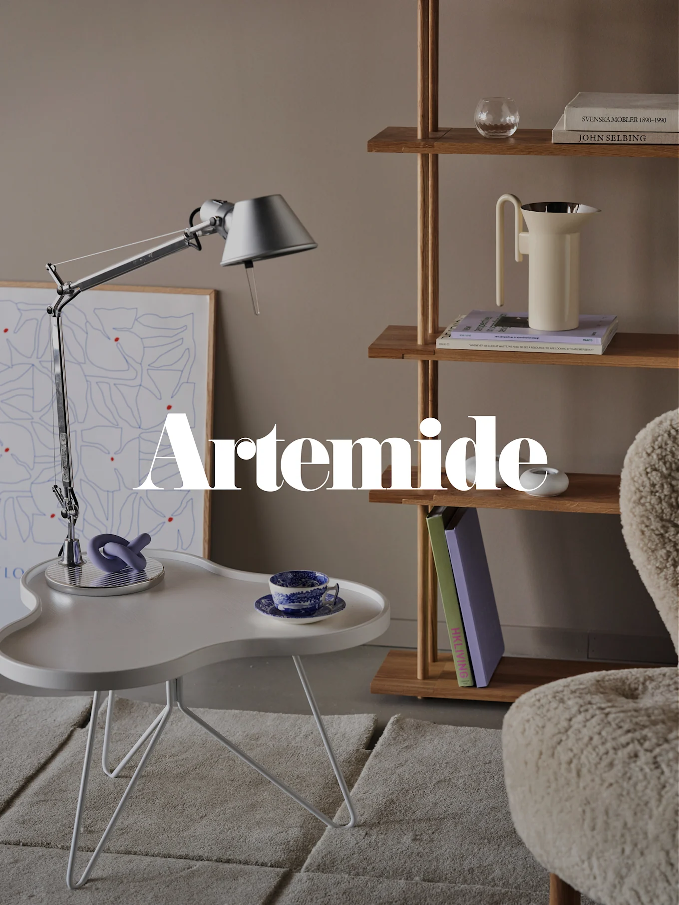 En moderne stue med en sølvfarget bordlampe, hvitt sidebord, trebokhylle og en kremfarget lenestol. Tekstoverlegg: 'Artemide'.
