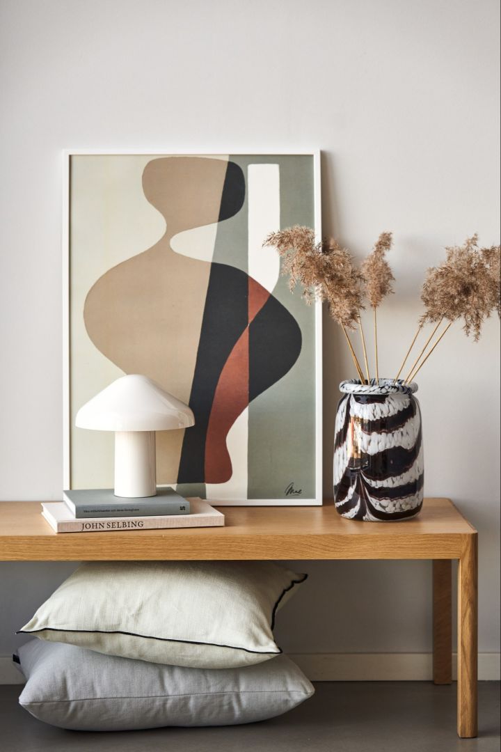 La Femme 03 poster fra Paper Collective, Hvit Pao portable bordlampe, Splash Roll Neck vase i hvitt og rødt fra HAY på en benk.
