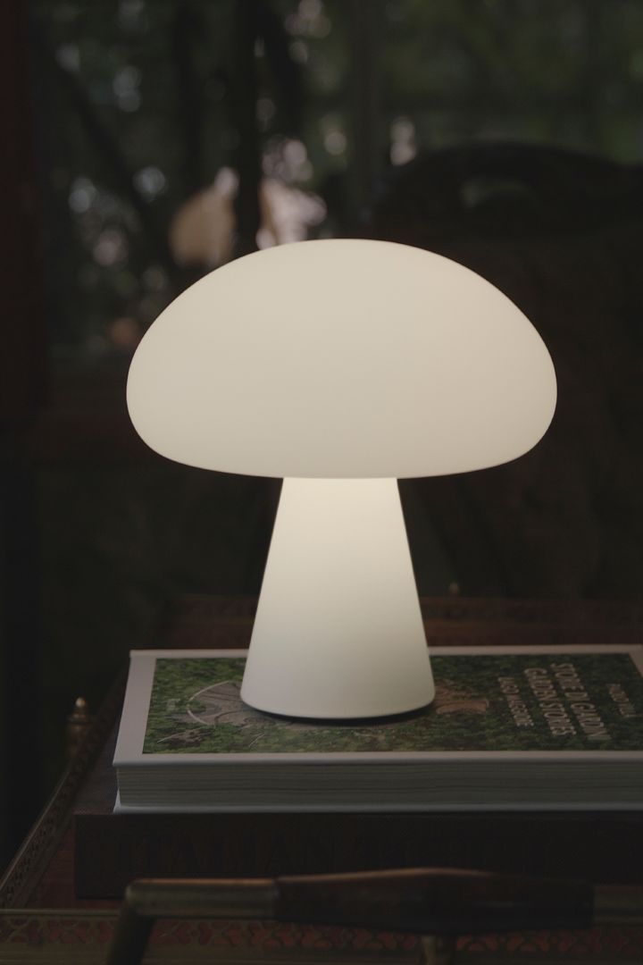 Den bærbare bordlampen med sopp i frostet glass fra GUBI står på et magasin ute i mørket.
