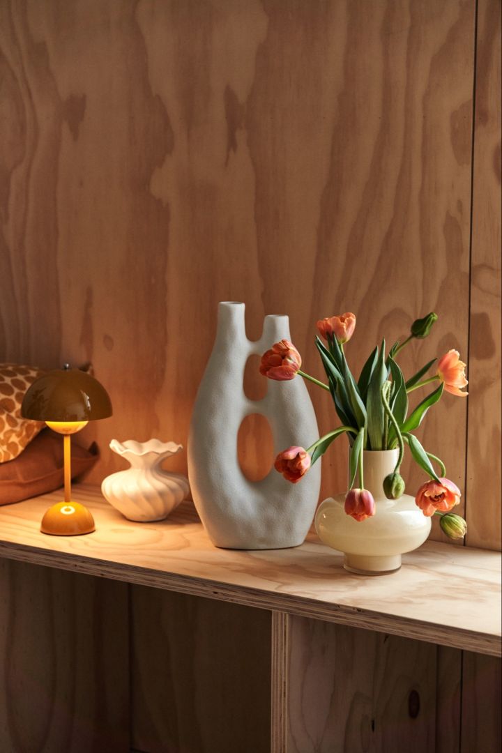 En avsats med en bærbar lampe, skulptur og en vase med blomster for å skape visuell interesse i et rom.