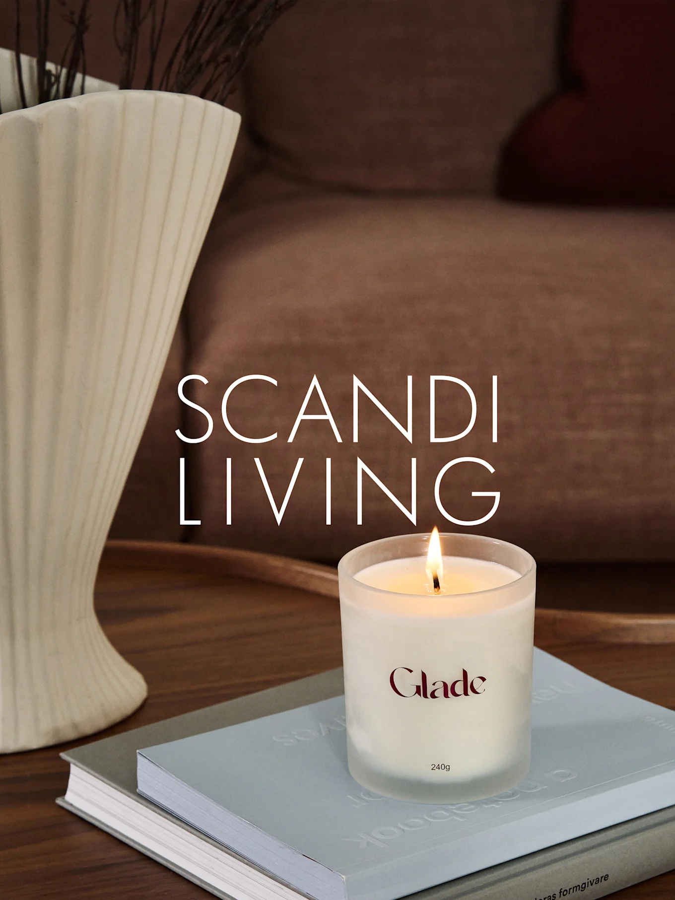 Et brennende Glade-lys på bøker, ved siden av en riflet vase med grener. Overlagstekst: SCANDI LIVING.