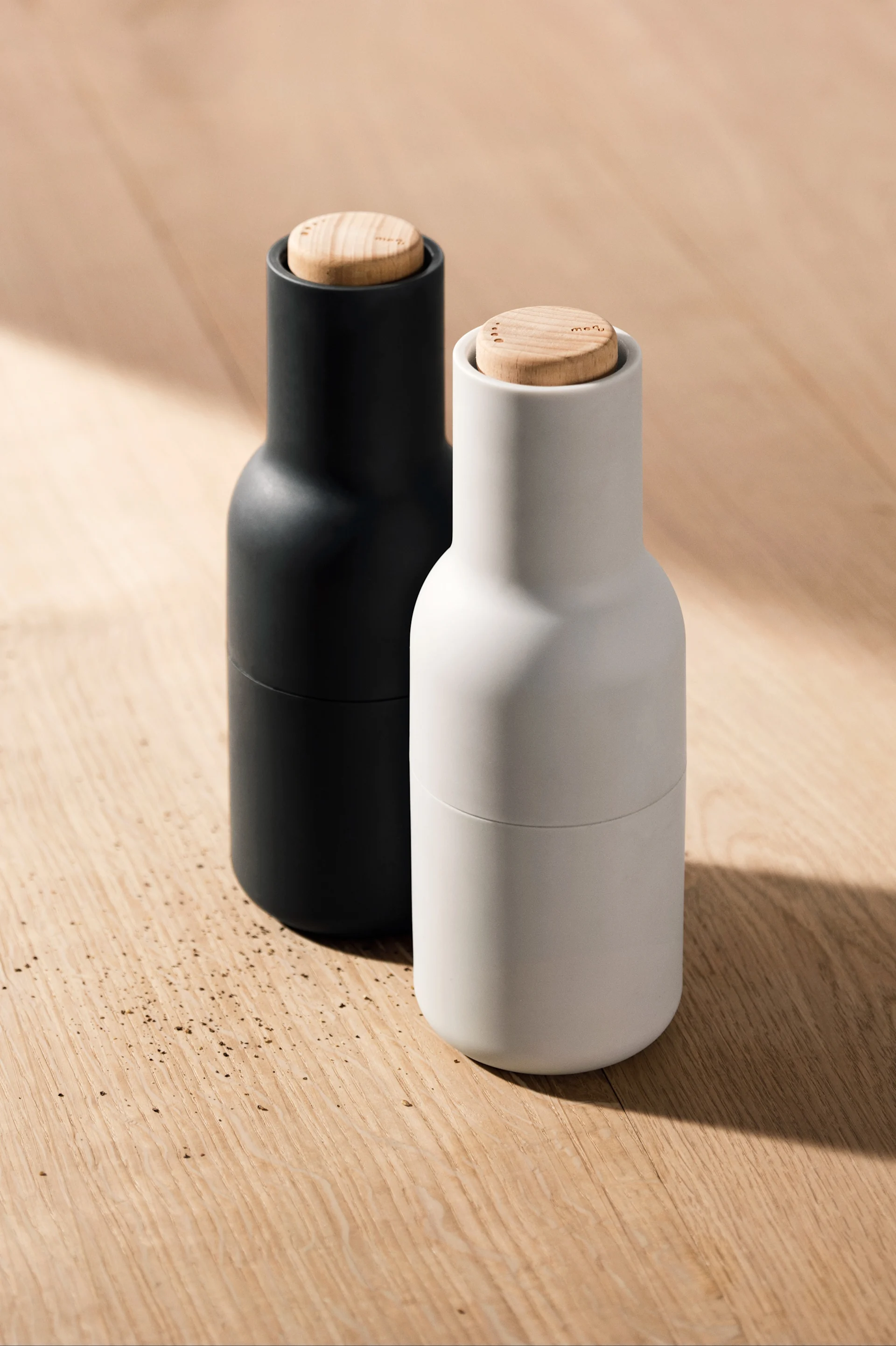 To Bottle Grinder-kverner fra Audo Copenhagen, plassert på et trebord.