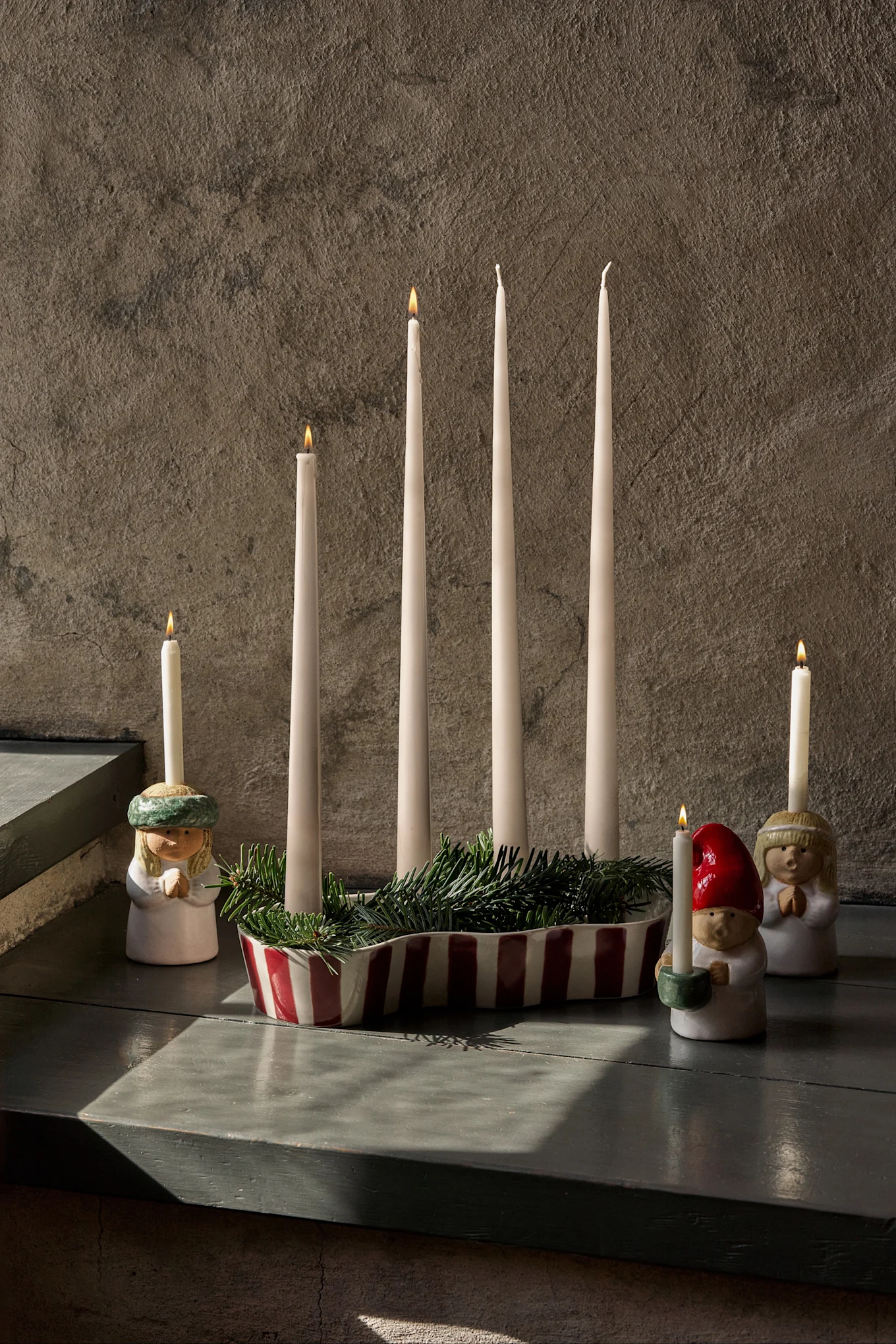 Adventsdekorasjon med fire uantente lys, grønt granbar og tre figurer som holder tente lys.