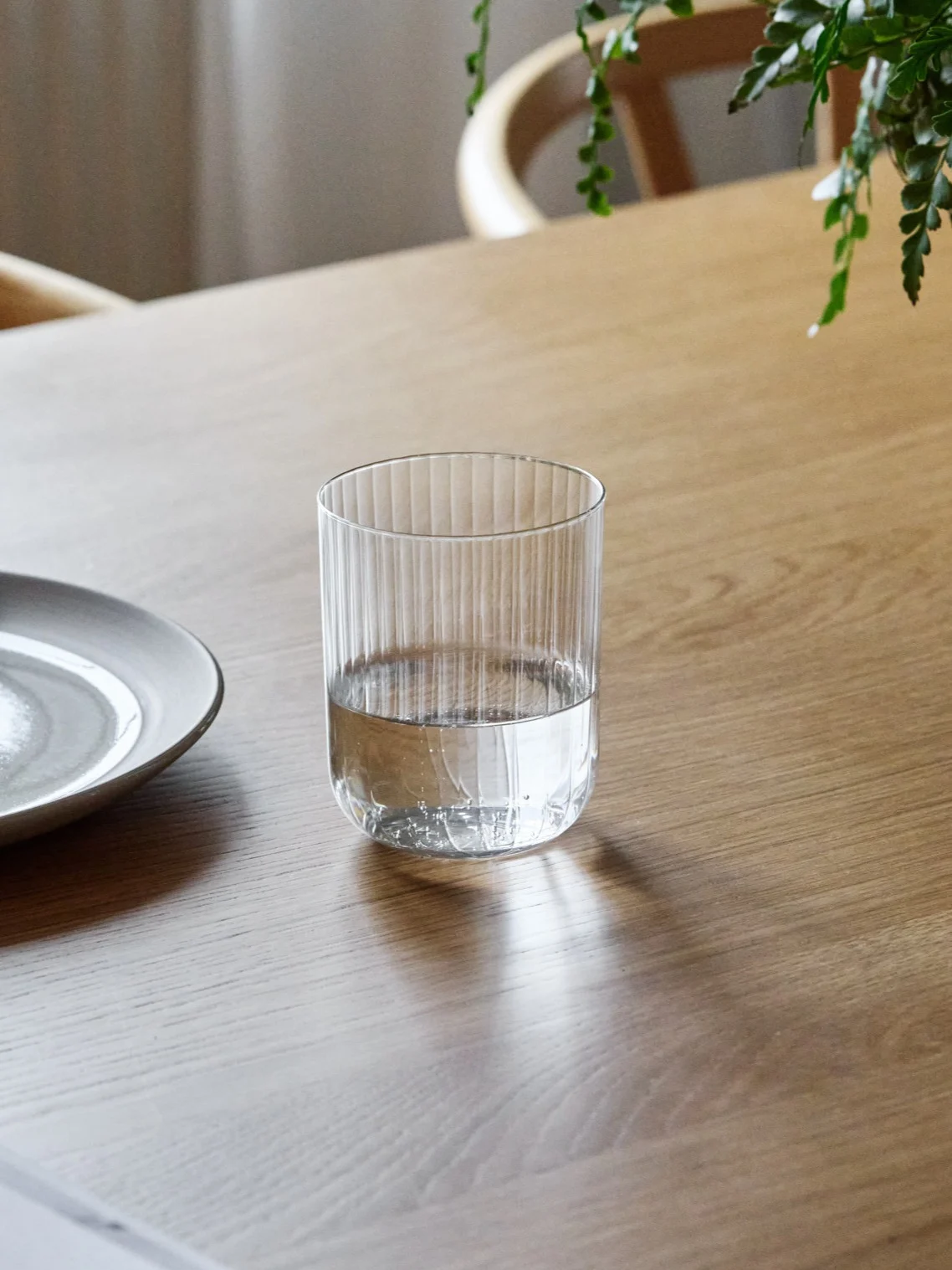 Et riflet glass, halvfullt med vann, står på et trebord ved siden av en keramisk tallerken.