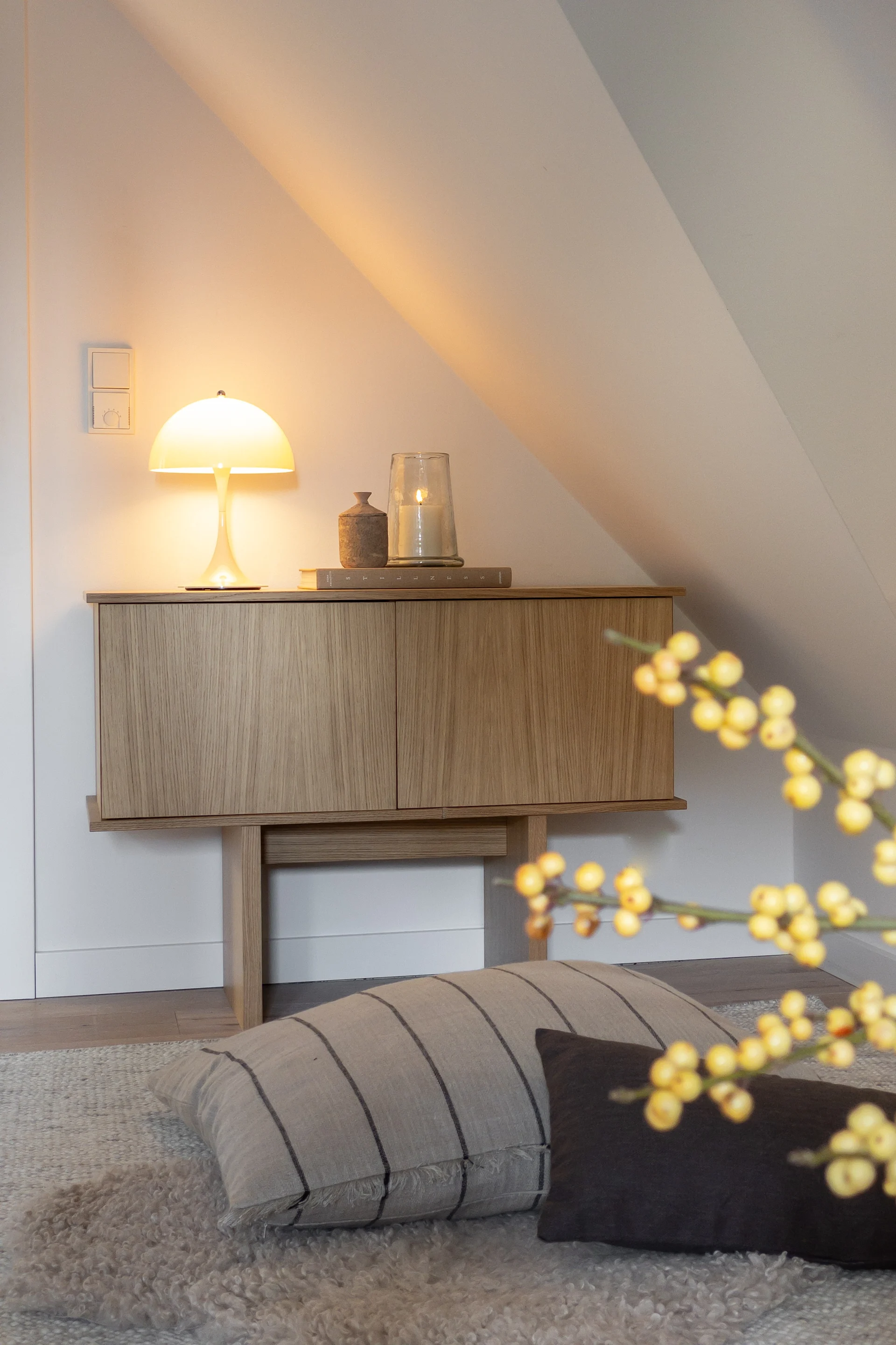 Et treskap med en glødende sopplampe og et tent lys, plassert mot en hvit, skrå vegg i et koselig rom.