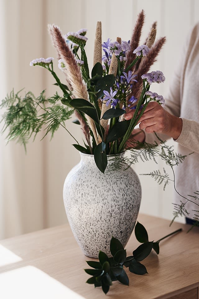 Hvit, høy vase i keramikk fra Knabstrup Keramik står på bordet med snittblomster fra Blombruket. 